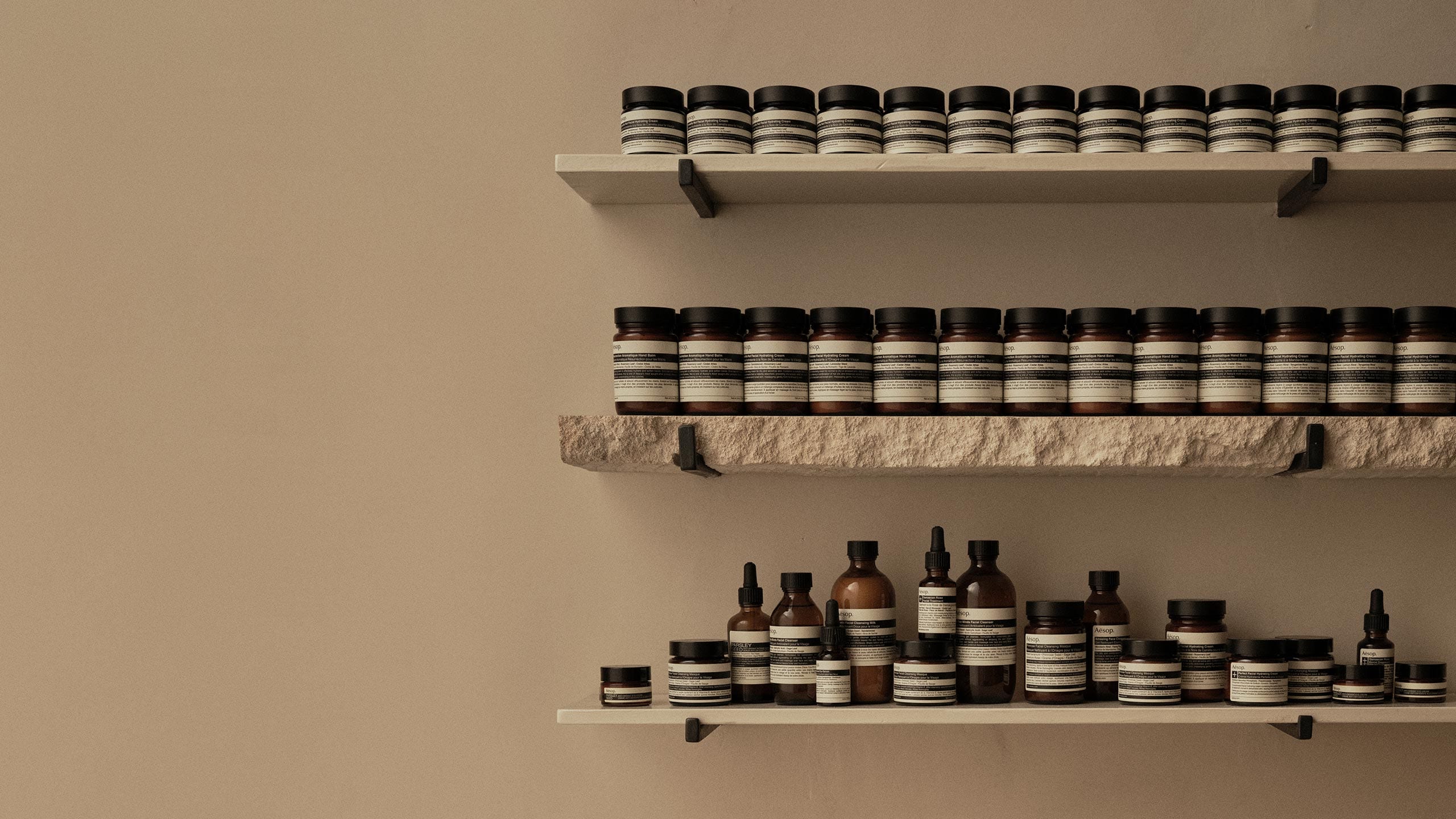 A sink and shelving made of stone, adorned with Aesop bottles and jars.