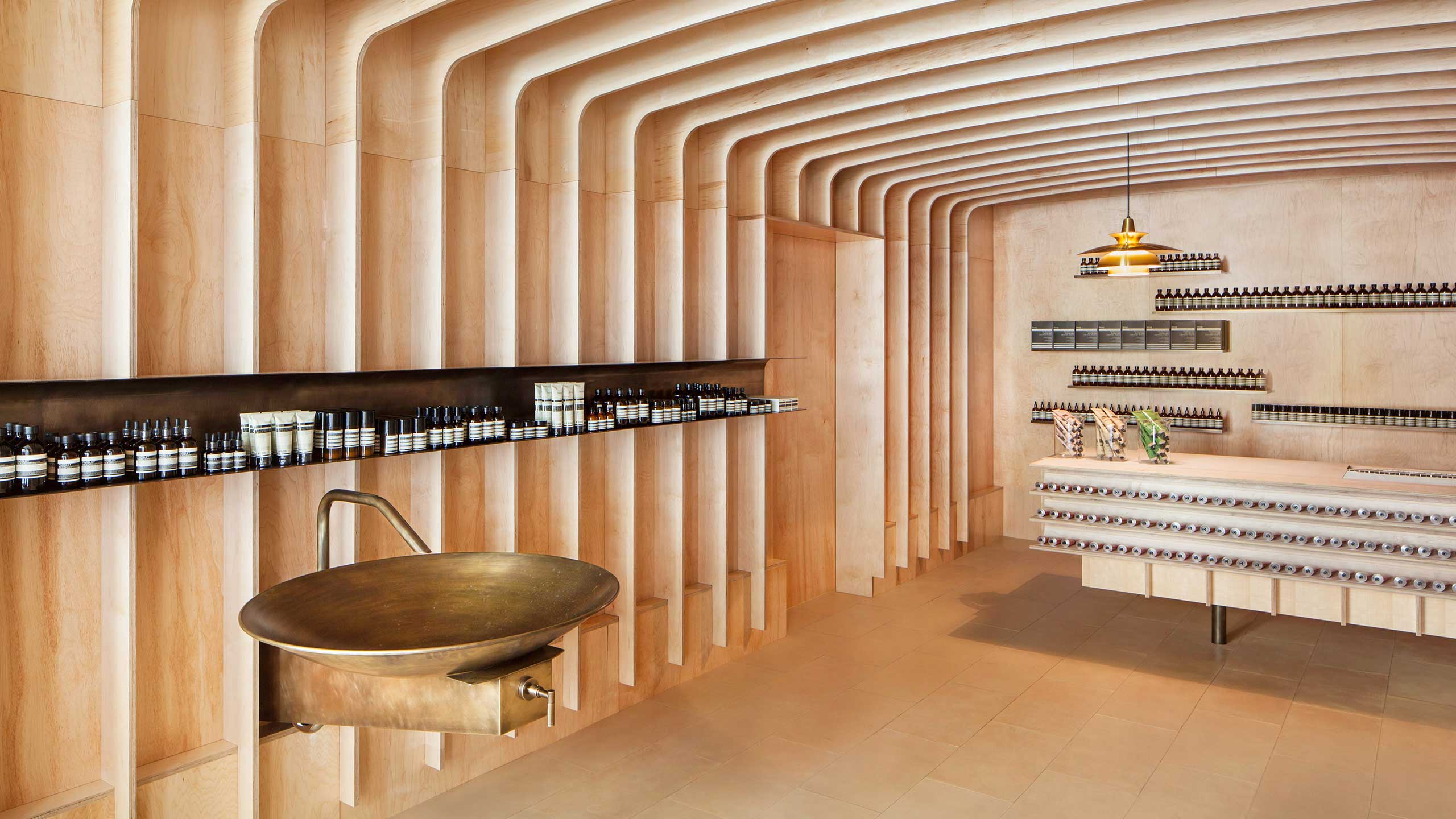 Brass sink with Aesop tester products on a brass shelf.