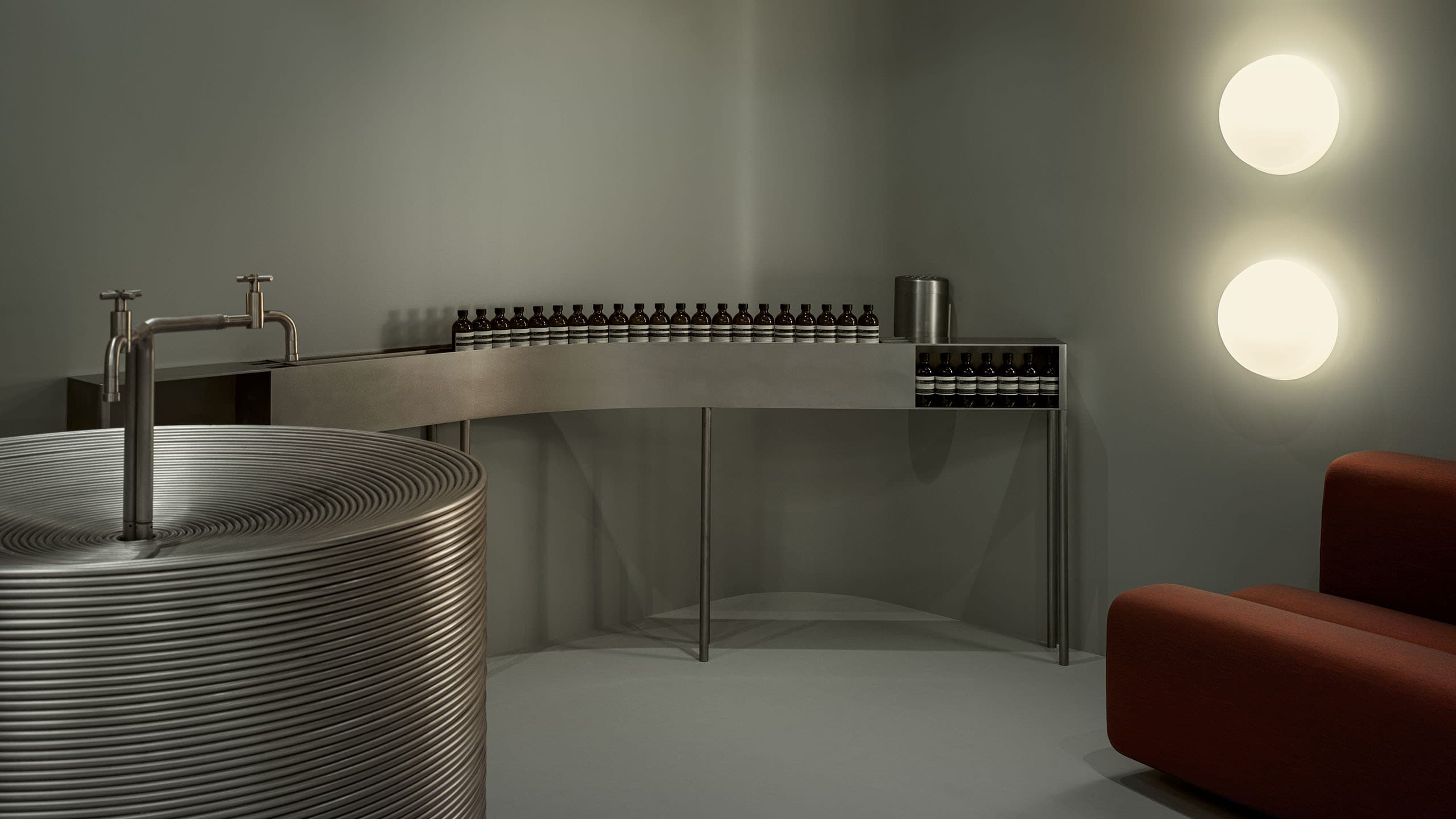 grey interior featuring steel coiled sink, partial view of red couch, and stacked round lights with product on steel table