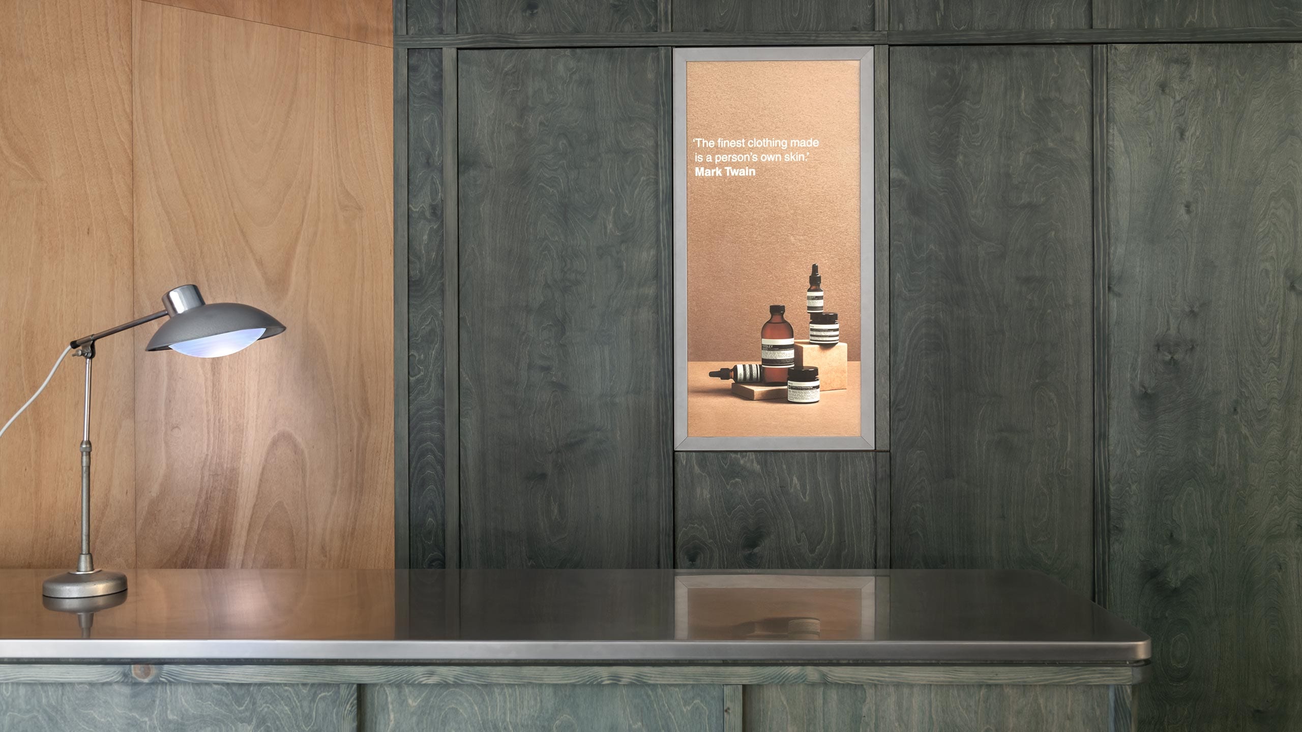 A metal lamp on a bench top placed in front of green and brown wooden walls