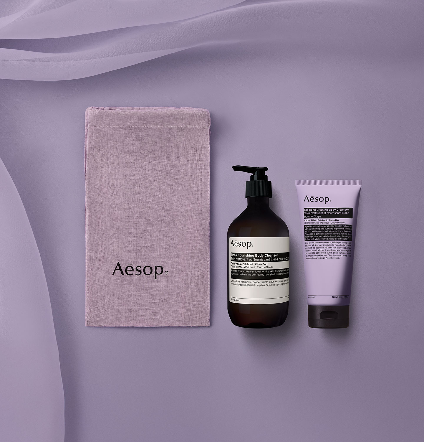 Eleos Nourishing Body Cleanser alongside the hand-dyed purple cotton bag placed on a flowing fabric lavender background