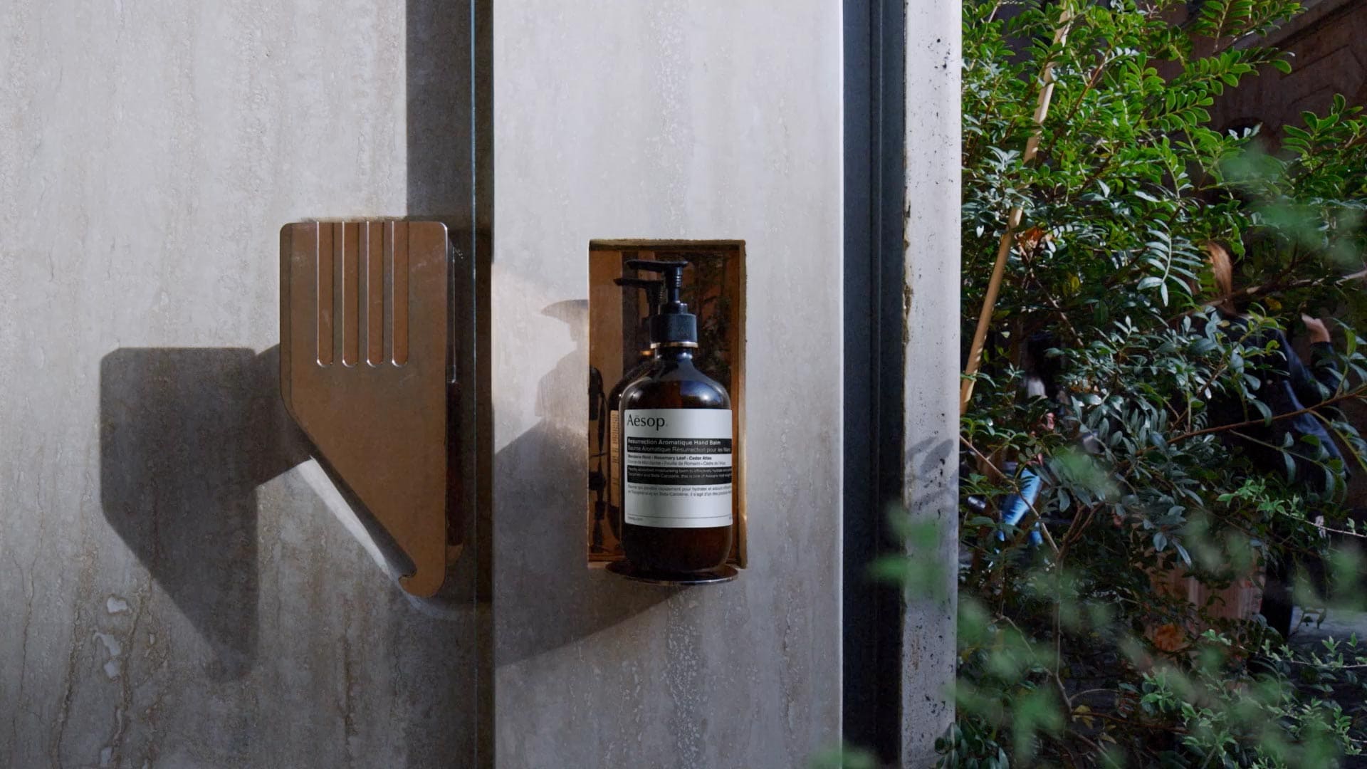 Resurrection hand balm in amber bottle with pump placed on a stand next next to a door and street.