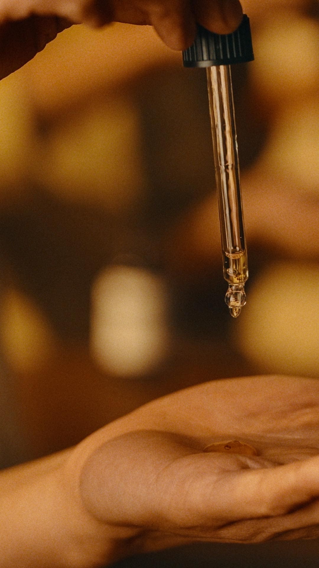 A hand holding a pipette dropper and squeezing a product on to another hand