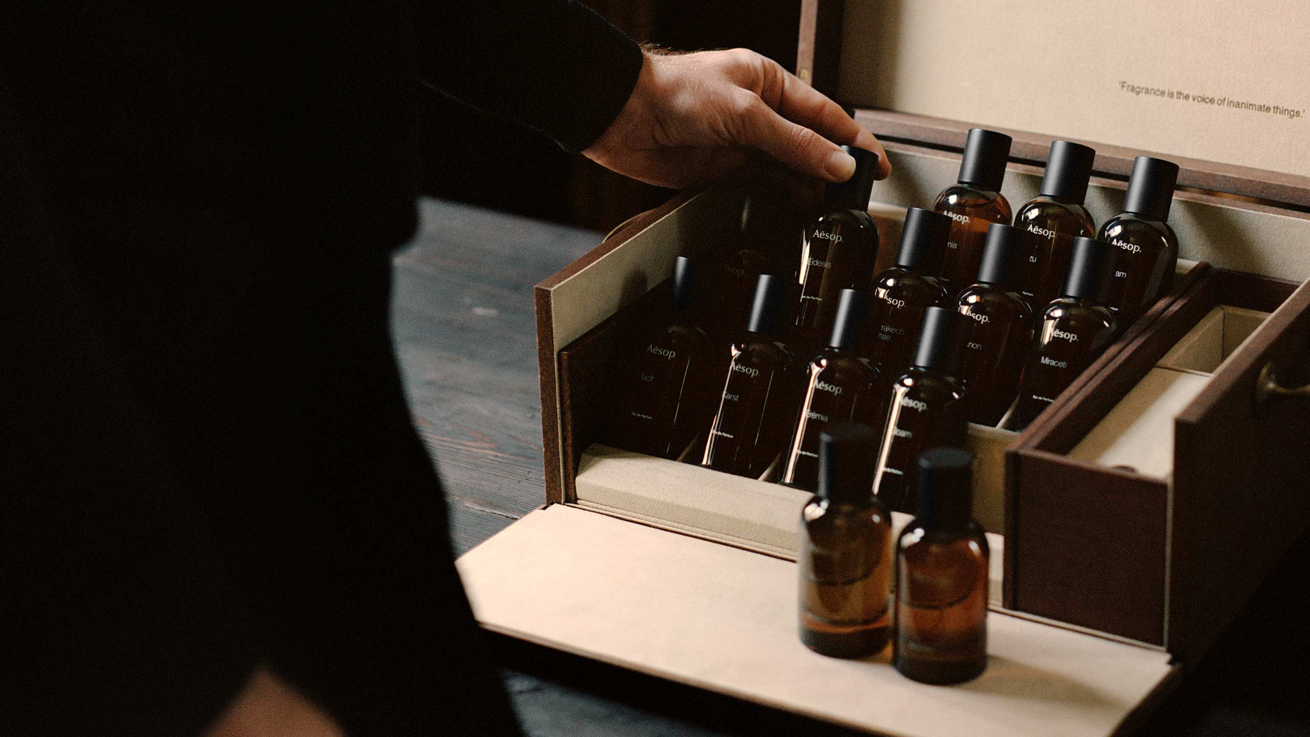 A hand grabbing Aesop fragrance in amber bottle from a wooden box