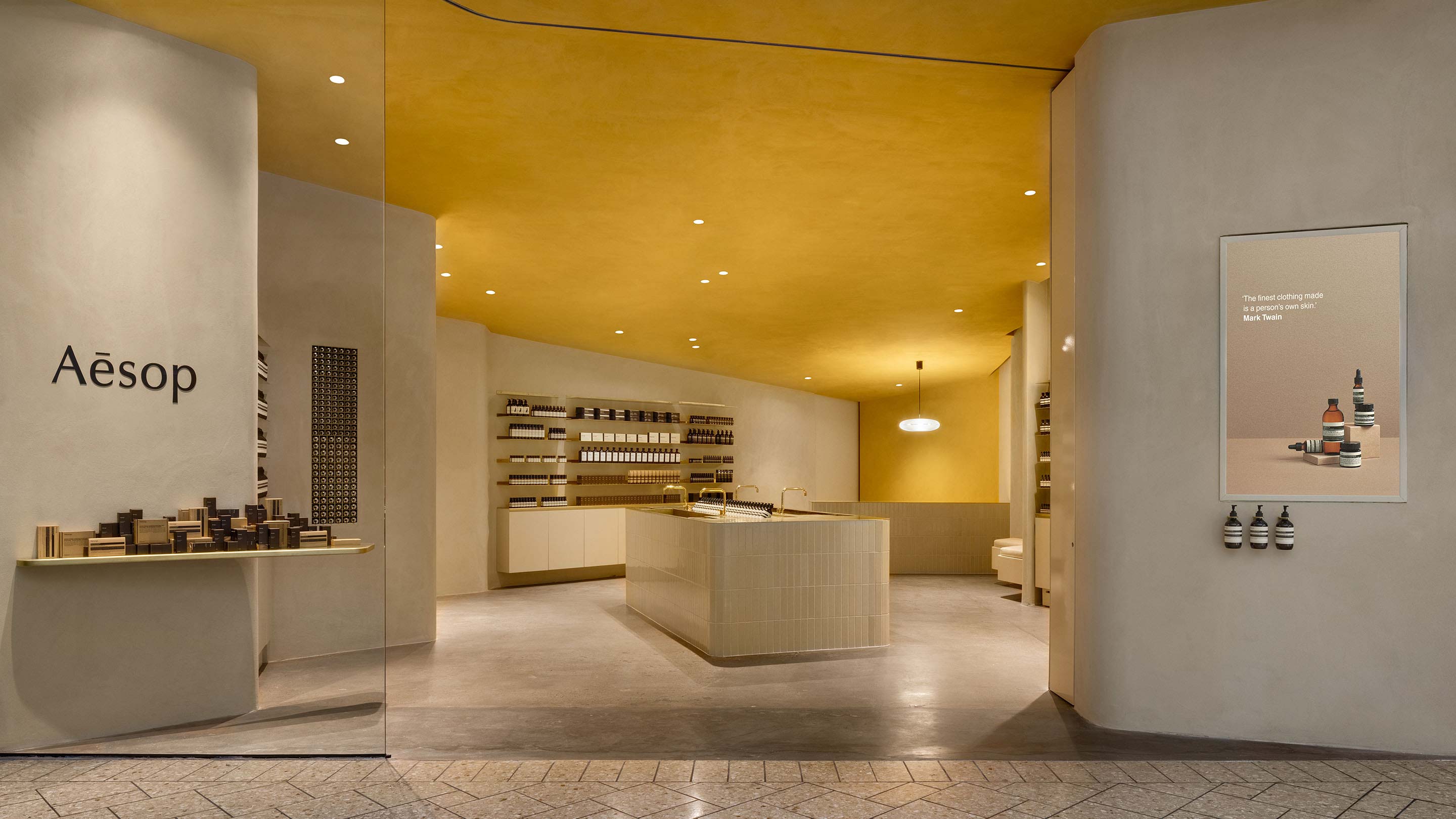 A minimalist concrete store interior juxtaposed with a yellow ceiling; a tiled sink sits at the centre of the shop floor.