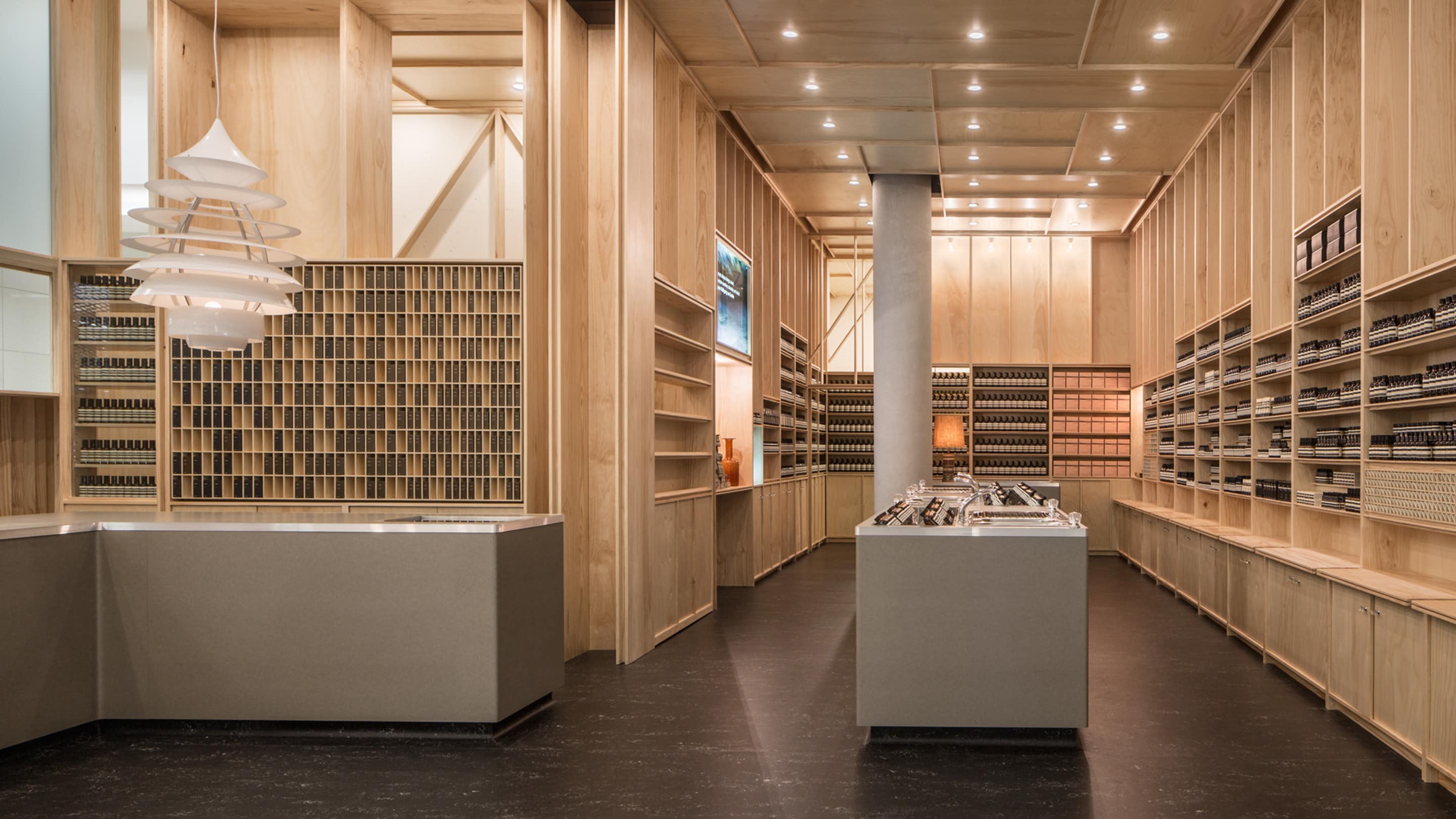 The interior is filled with natural wood and smooth grey counters. A concrete pillar is located in the back of the store.