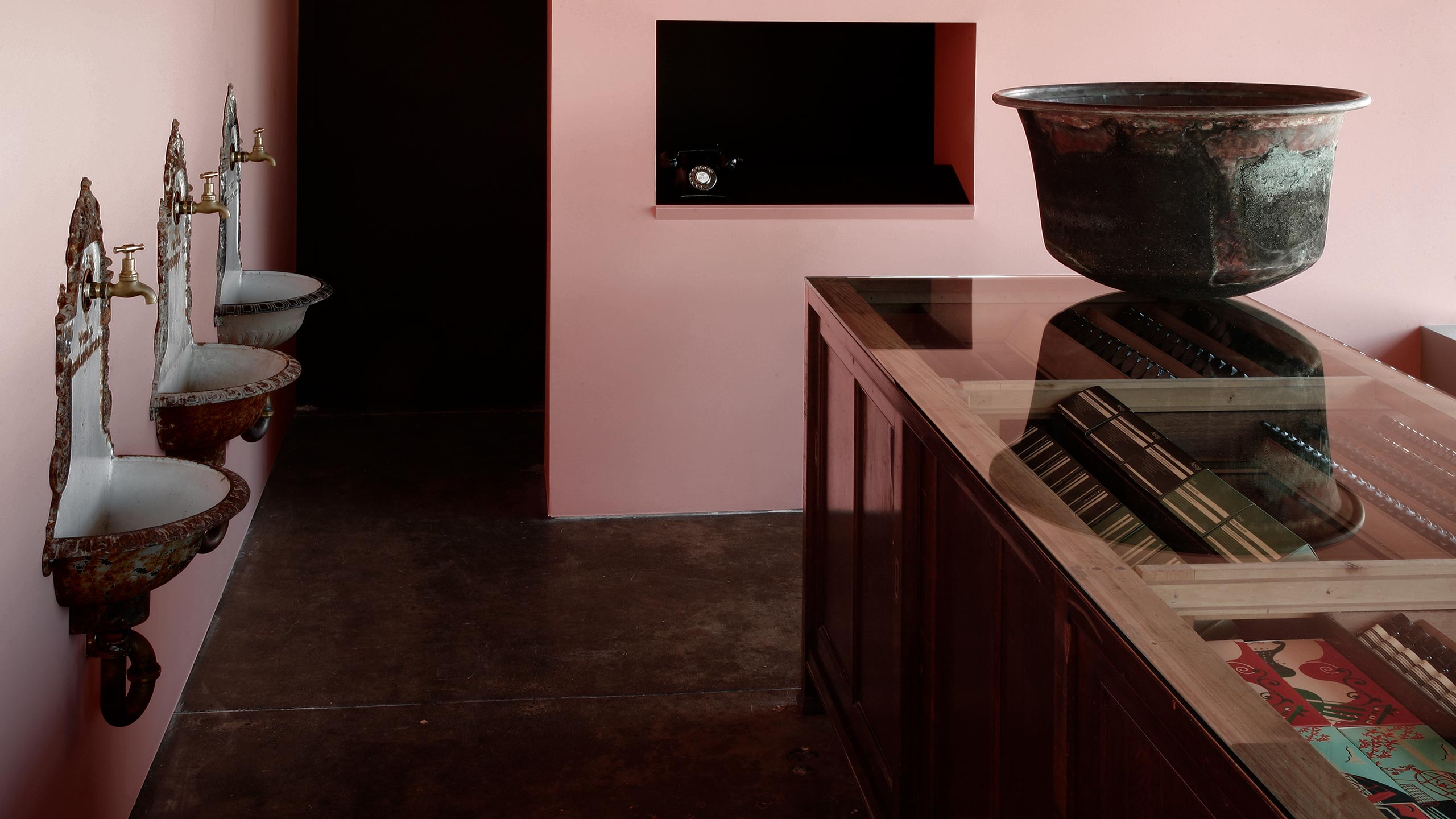Three vintage Viennese fountains are mounted to the wall on the left. On the right, the vintage, glass top counter hosts a vintage rusted basin.