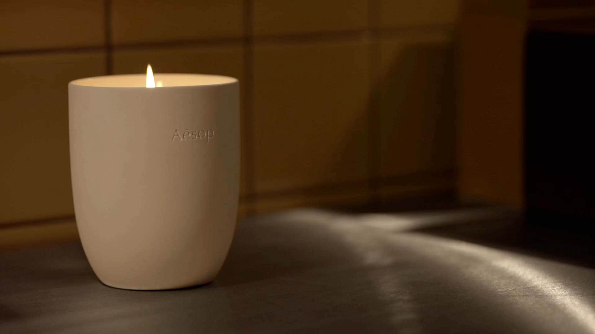 A lit candle in front of a tiled surface.