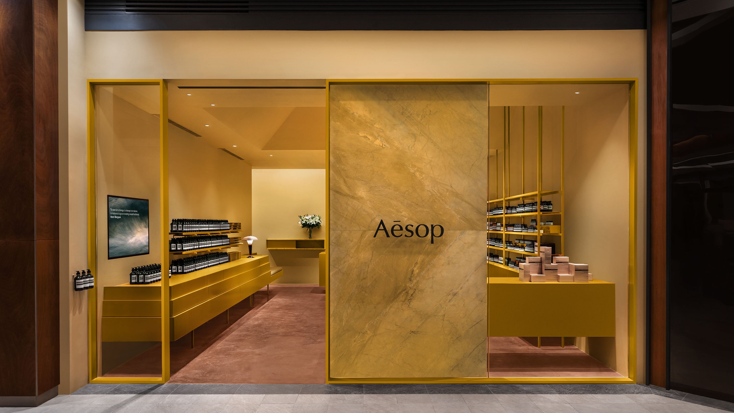 Store entrance to Aesop Rockwell displaying yellow framed windows and muted red carpet floors.