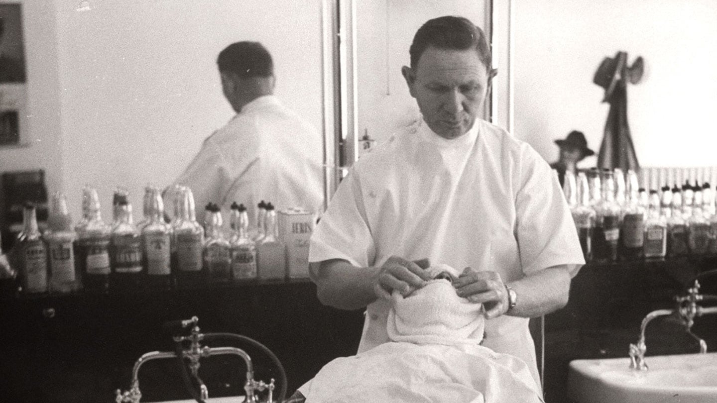 A black and white photo of a barber preparing for the grooming process with a customer at a salon