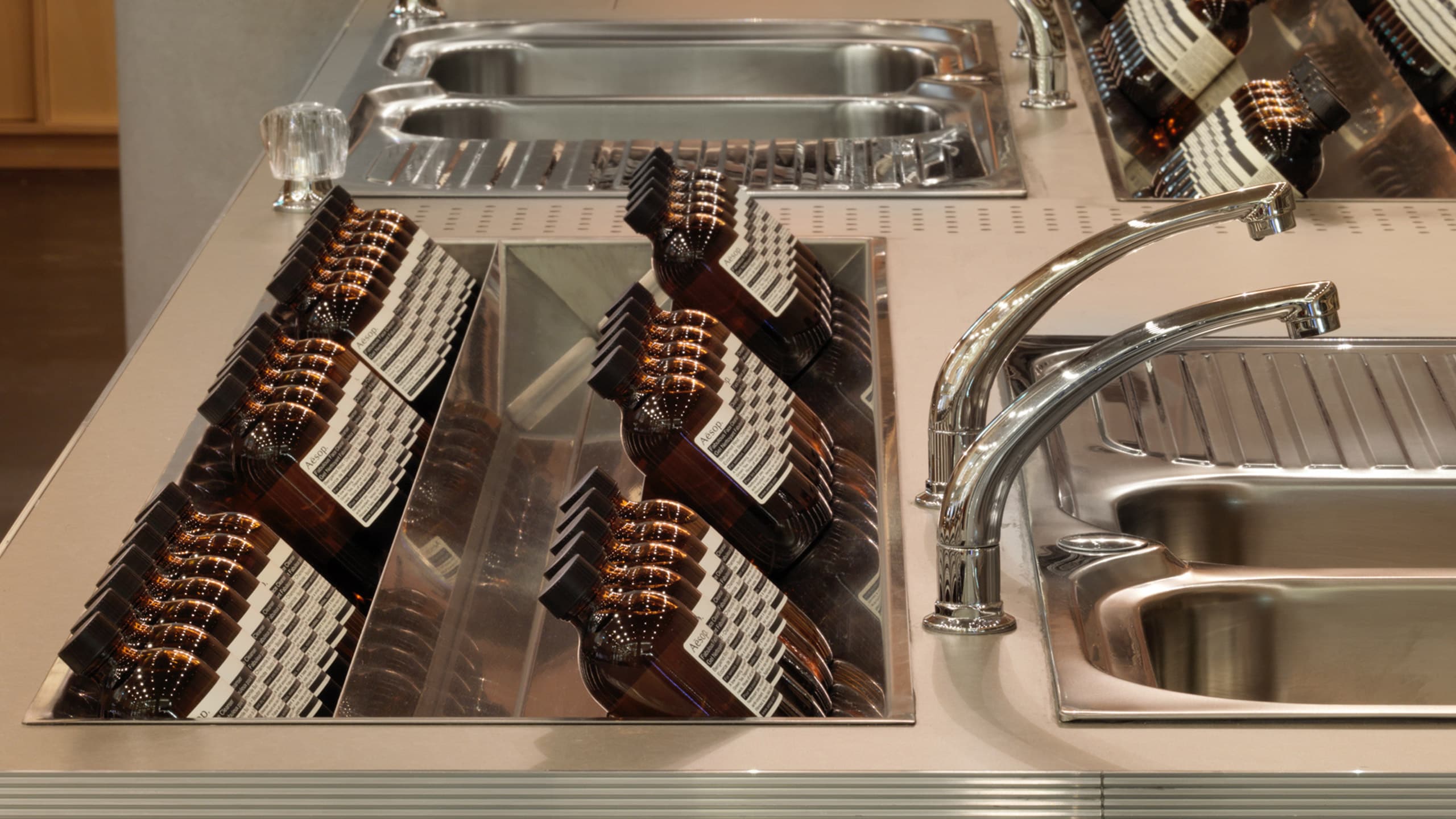 Stainless steel sinks and fixtures. There is a cavity int he counter-top that houses several Aesop bottles. 