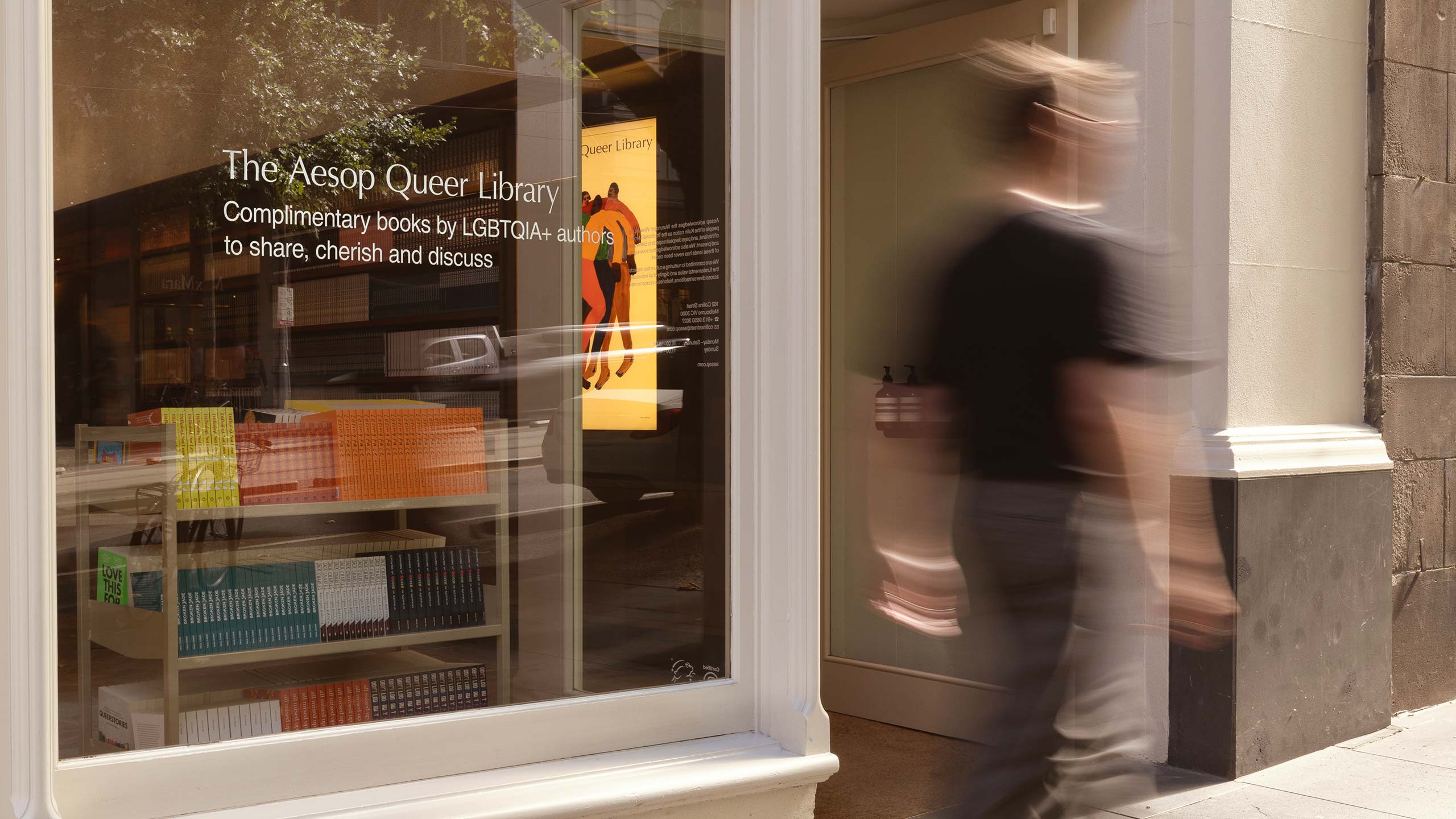 A blurred figure of a person walking past the Aesop Collins Street store, showcasing the shelves stocked with a range of books.