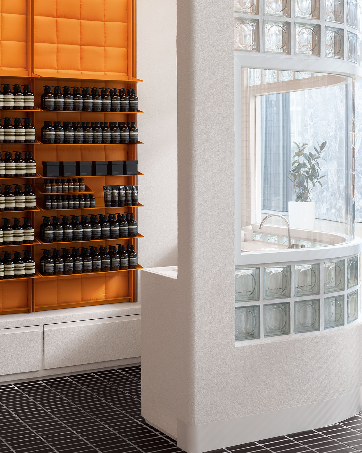 store interior featuring products in brown glass bottles on orange shelves, with swooping white wall and ceiling trim on the right