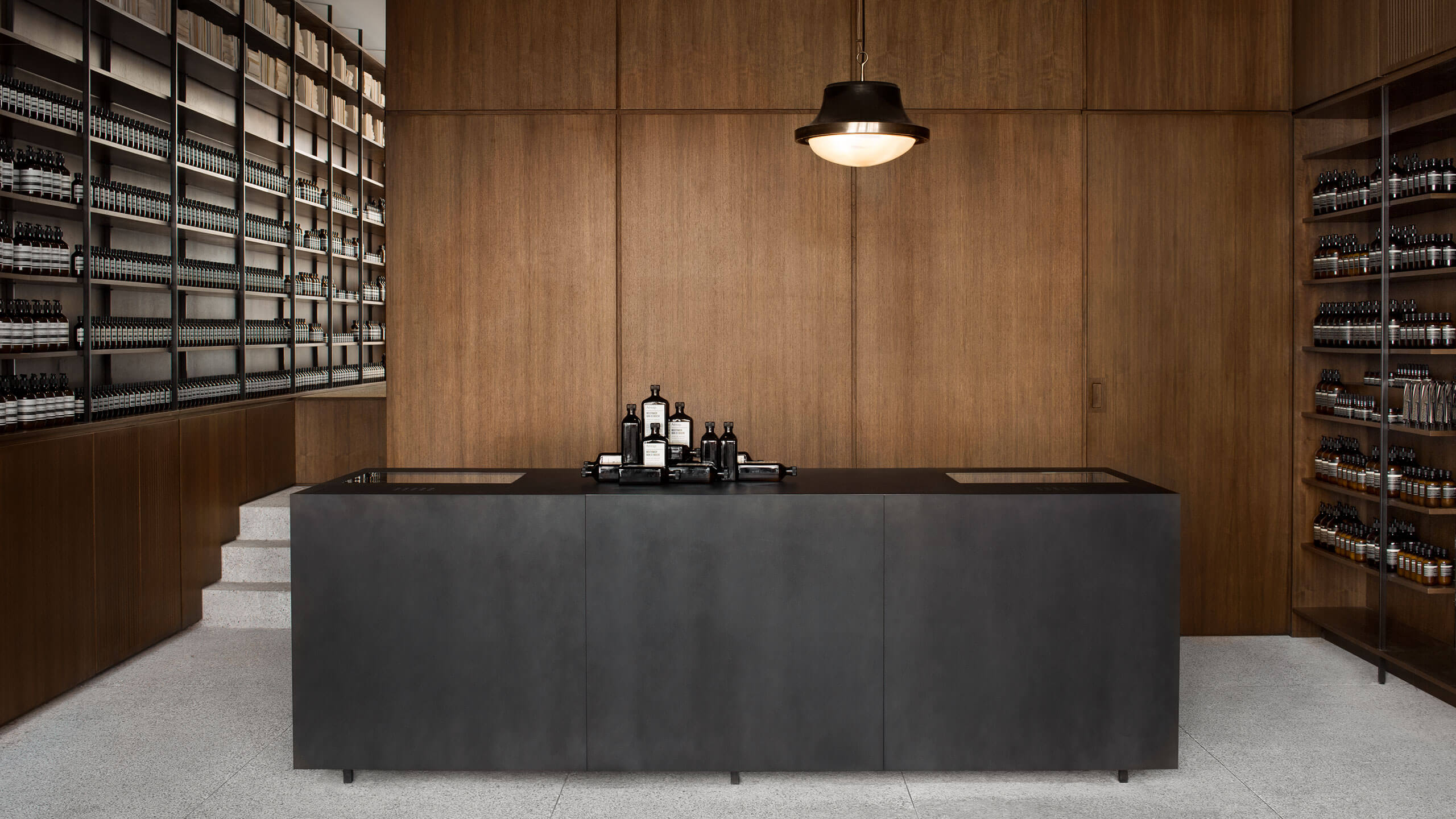 A steel black counter with Aesop Mouthwash glass bottles merchandised on top.