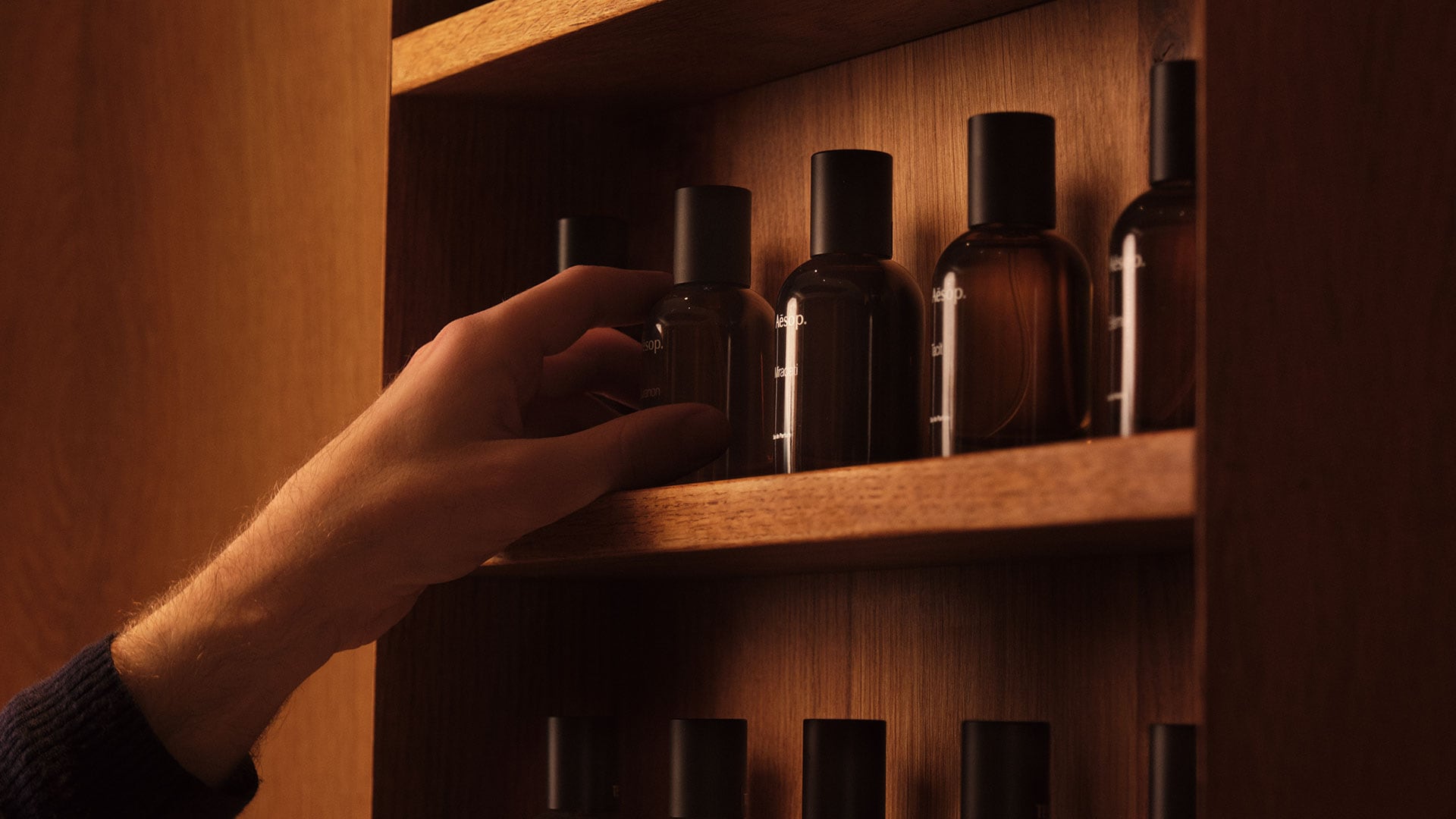 A hand touching a wooden shelves displaying Aesop fragrances