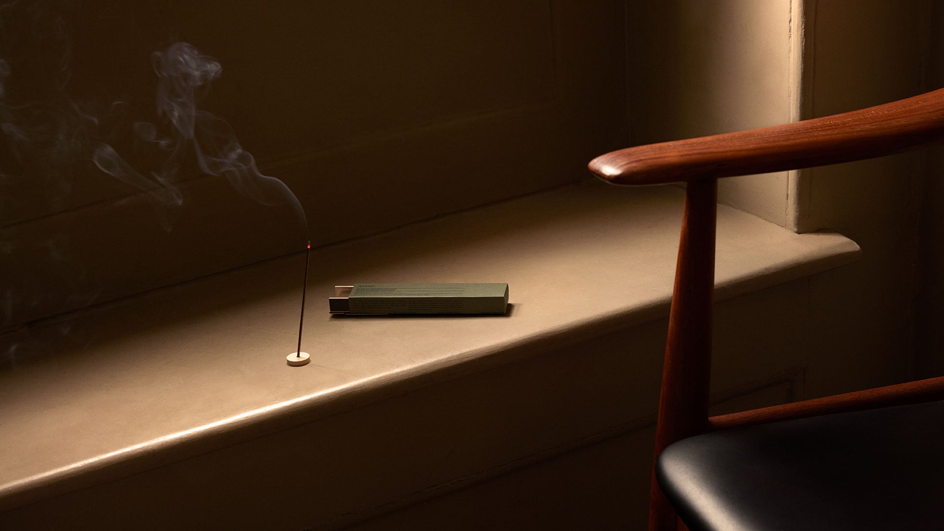 A lit stick of incense sitting alongside a mid-century chair.