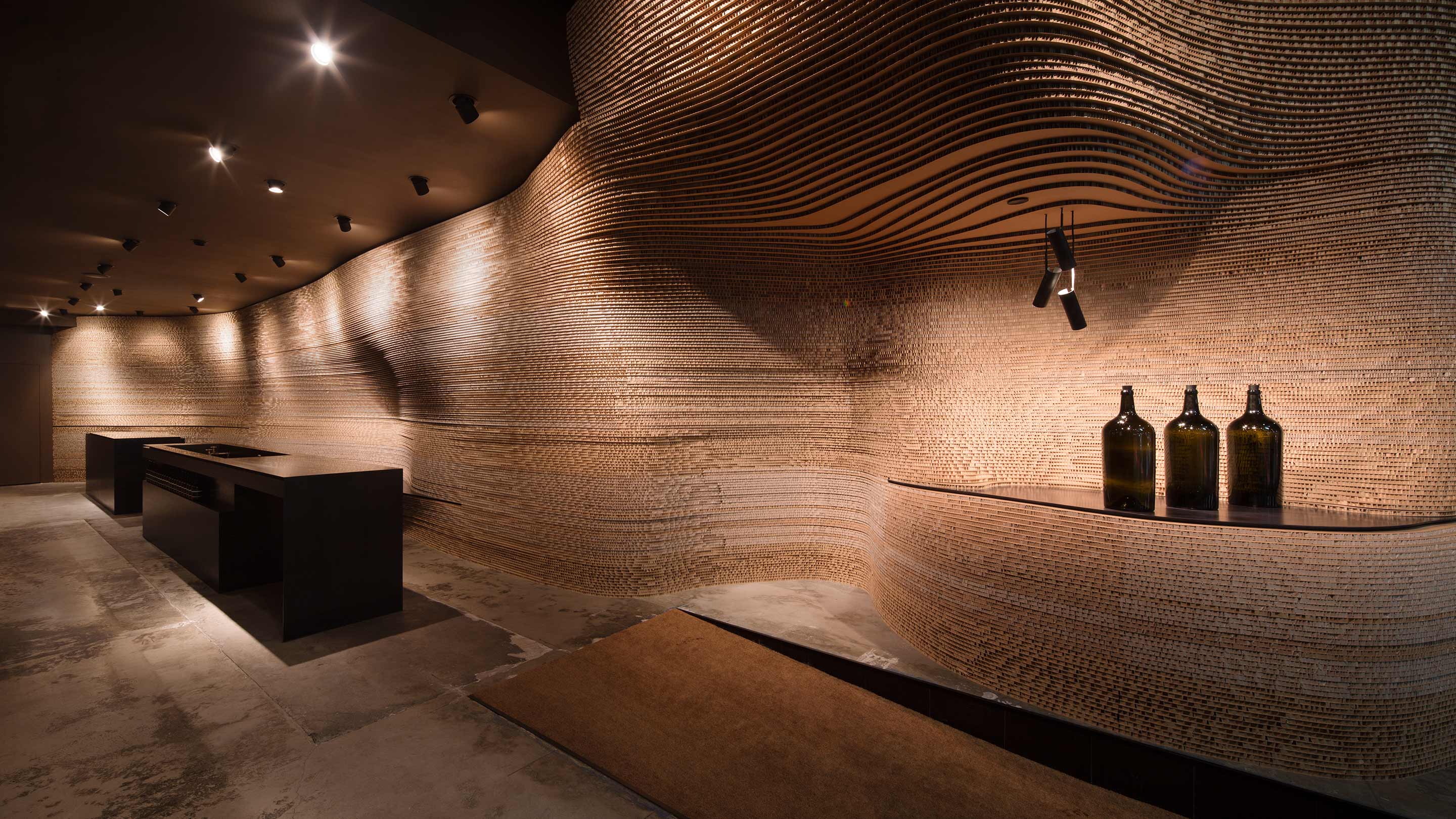 The right-hand wall crafted out of 1,550 industrial cardboard sheets. The flooring is blemished, polished concrete. The dark wooden customer service desk is on the left. 