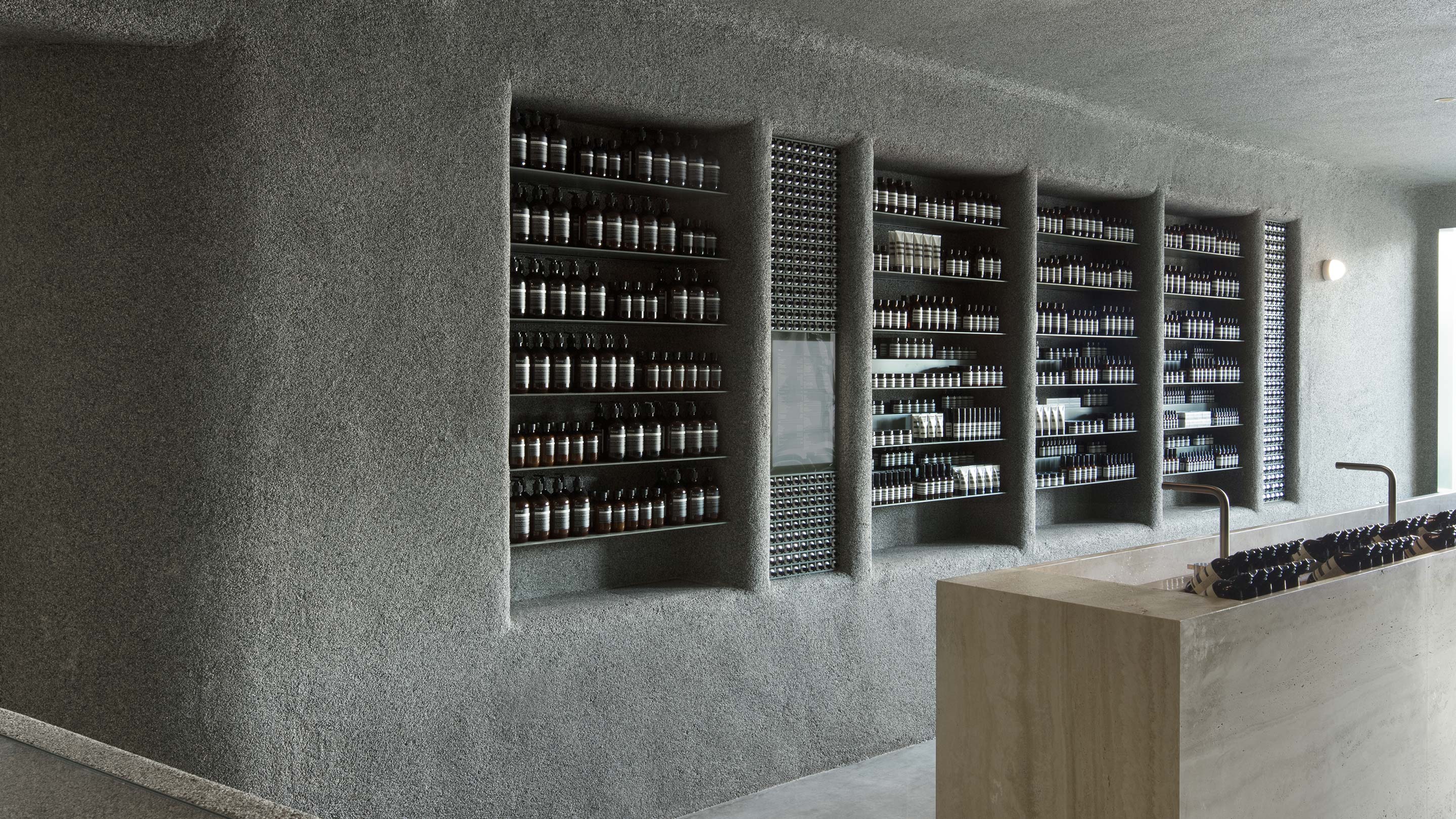 Textured concrete walls, shelves and ceiling with a timber basin and brass fixtures.