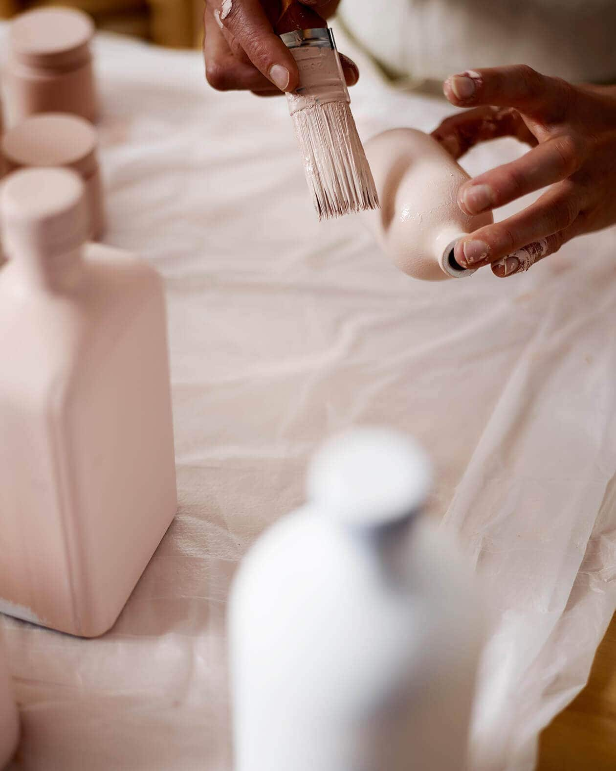 Primer plano de unas manos pintando de blanco un frasco de Aesop