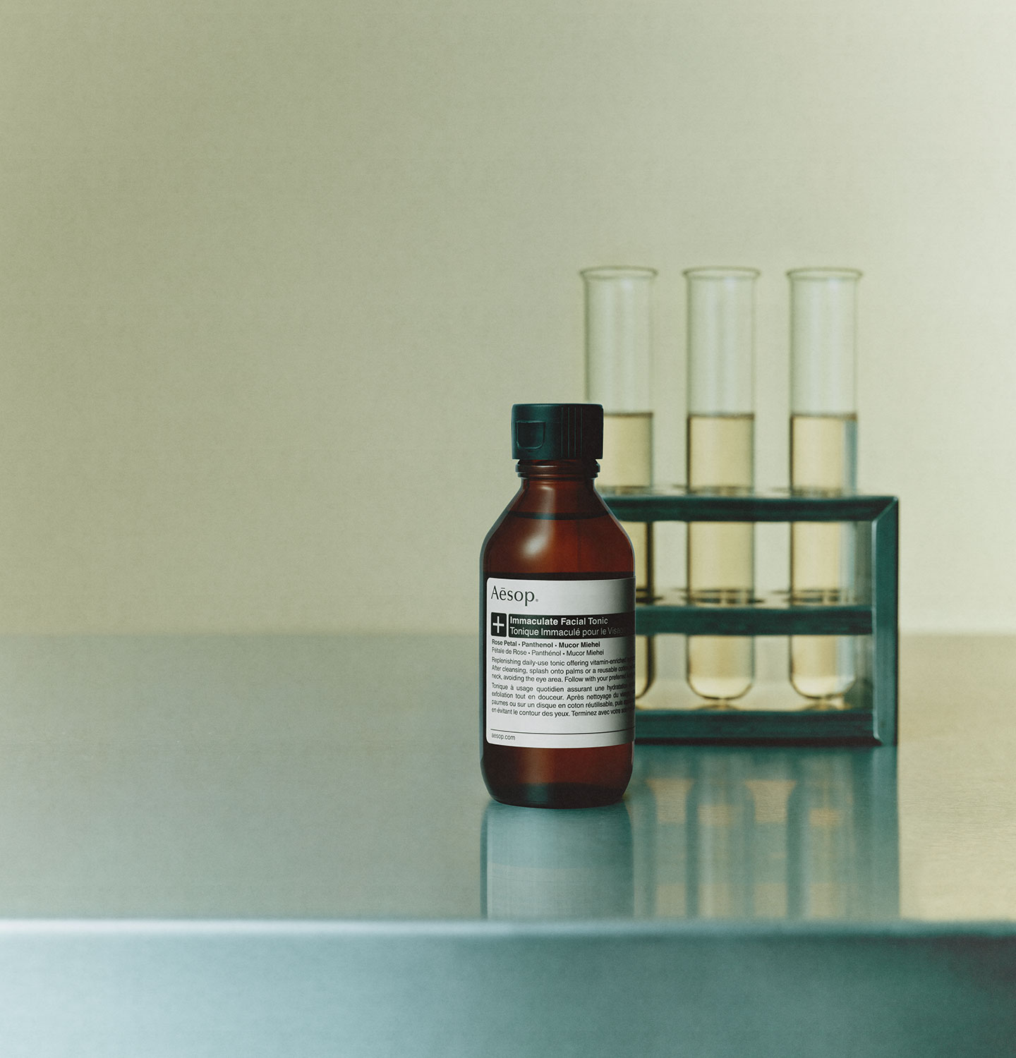 Immaculate facial tonic in amber glass bottle placed on metalic surface next to three test tubes