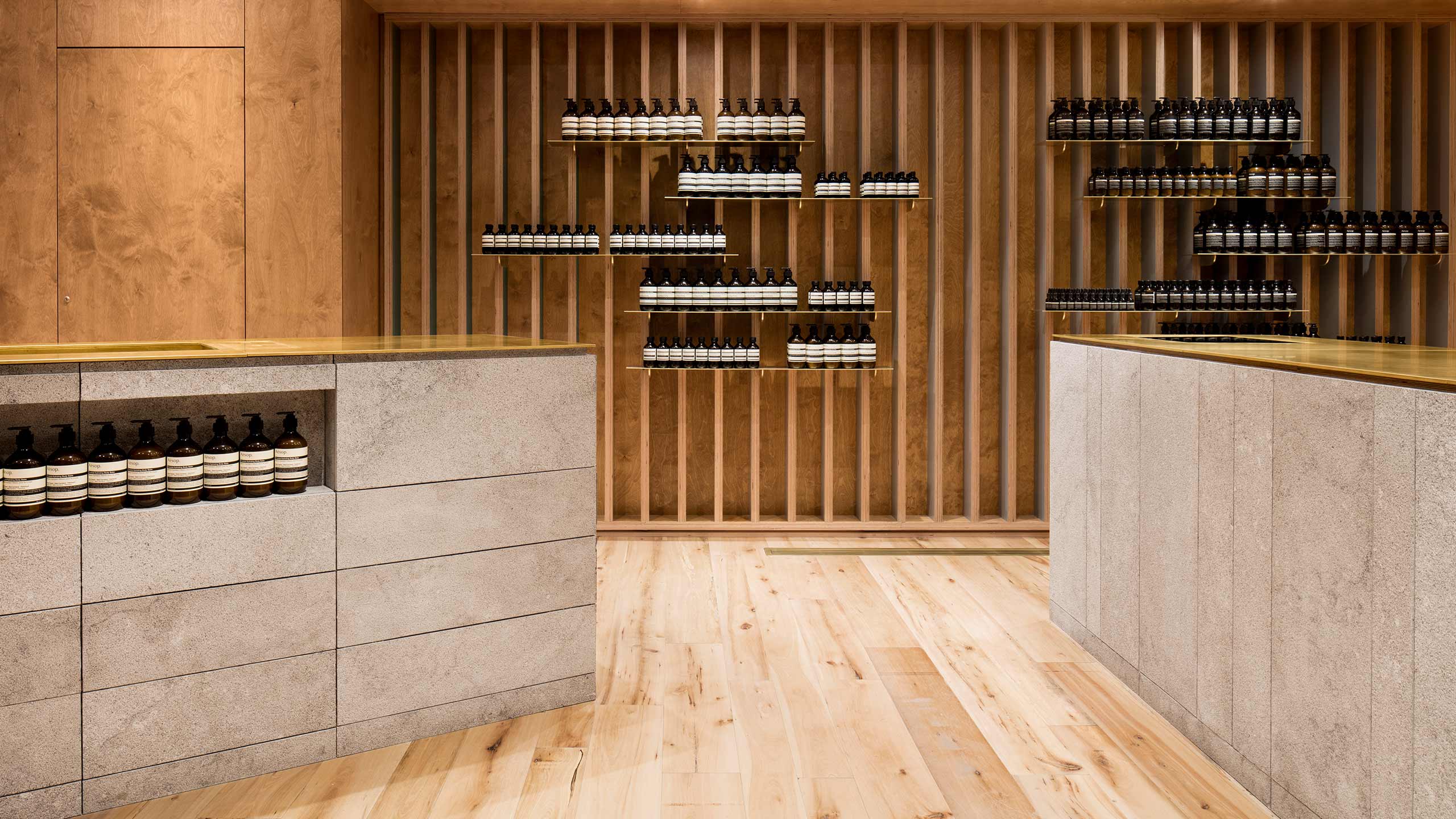 To the left, a large sink stocked with Aesop pump bottles; to the right, a large limestone counter with a view of the stud wall holding Aesop product.