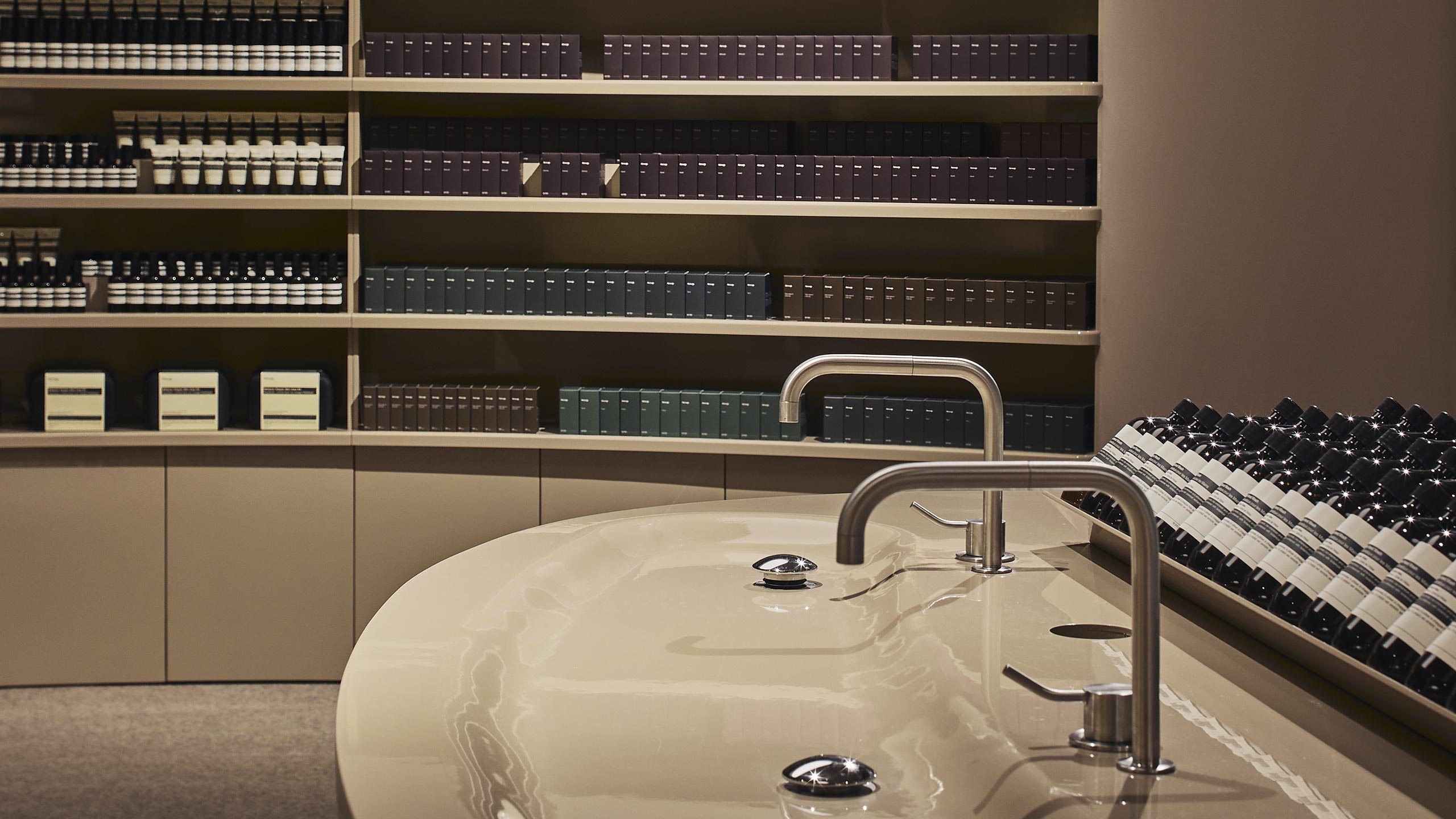 A glossy beige sinks in Aesop Miranda store, placed in front of shelves displaying Aesop products.