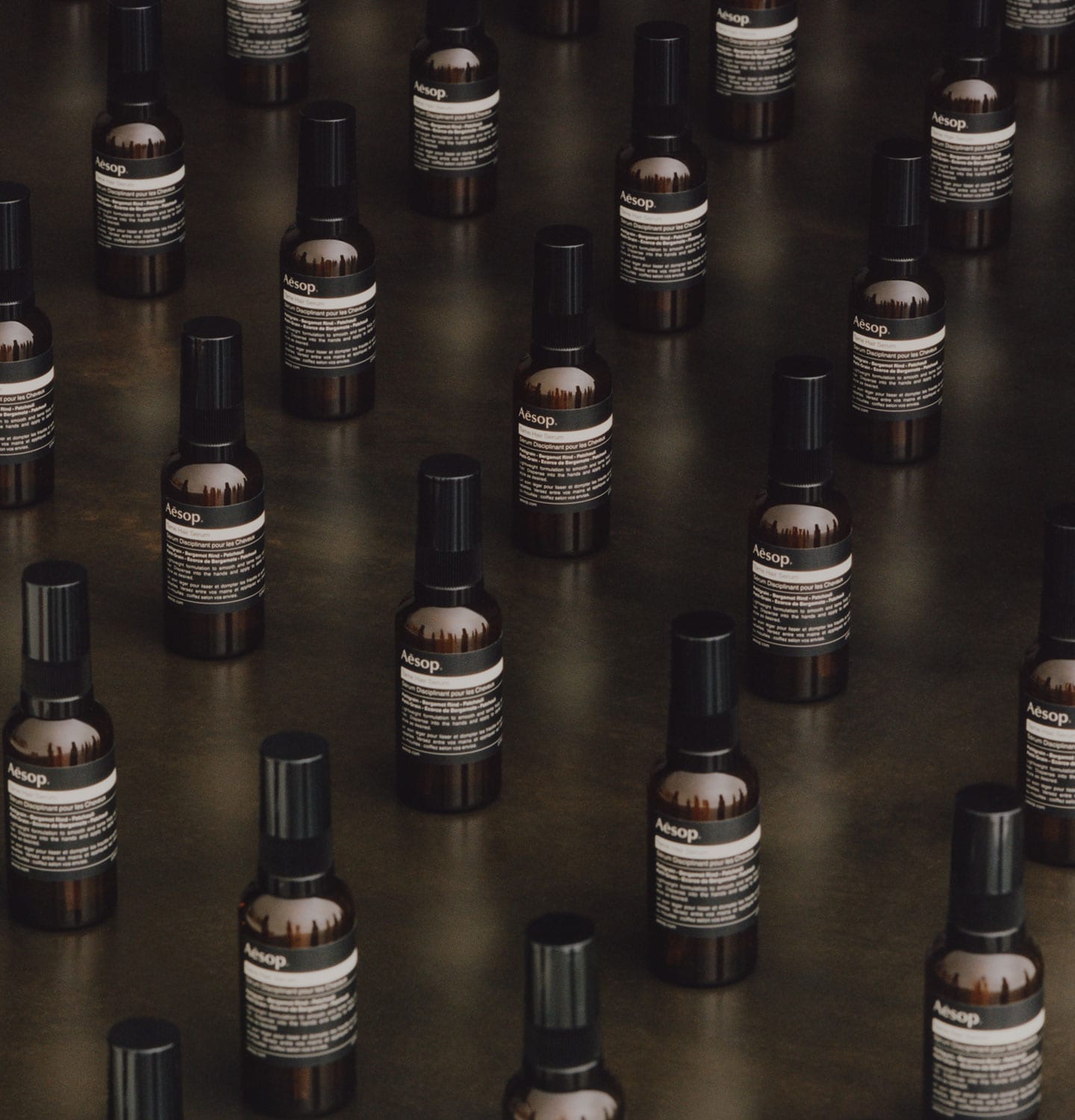 Frascos de Tame Hair Serum de Aesop colocados sobre una superficie de madera