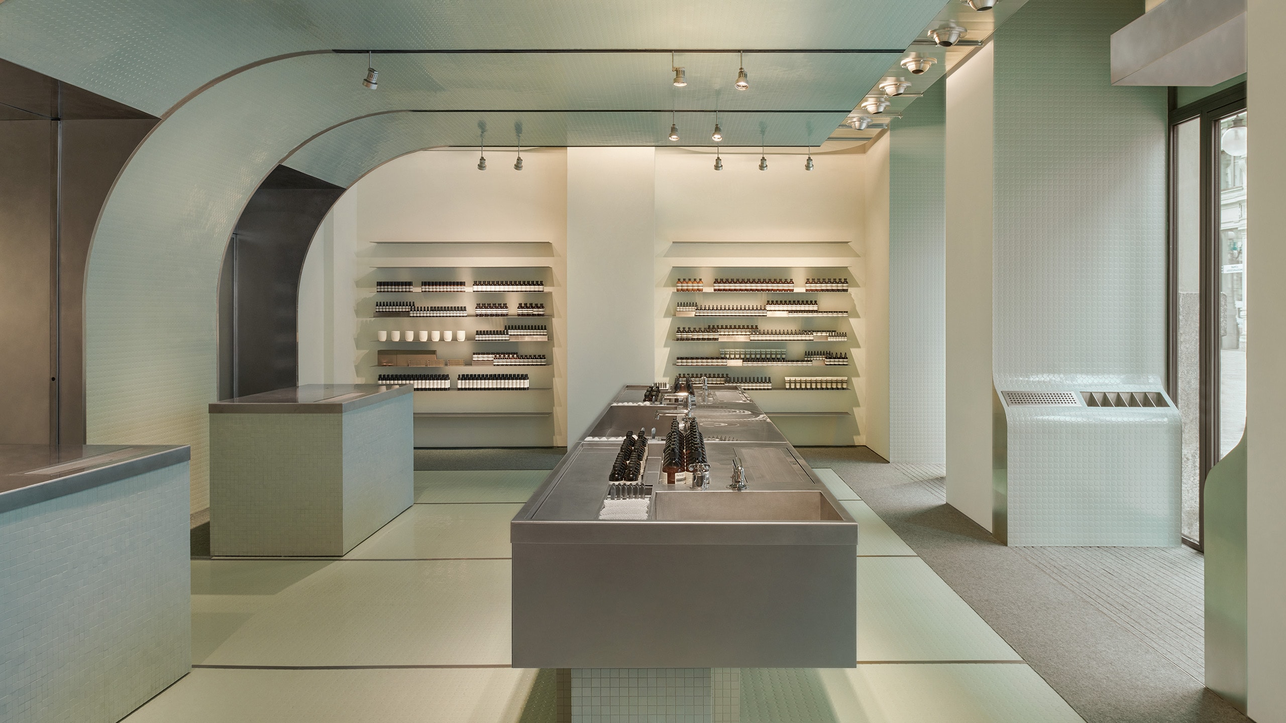 Aesop Milano Cordusio store interior made of rubber, stone and metal. Featuring the main basin and amber bottle product displays in the background.