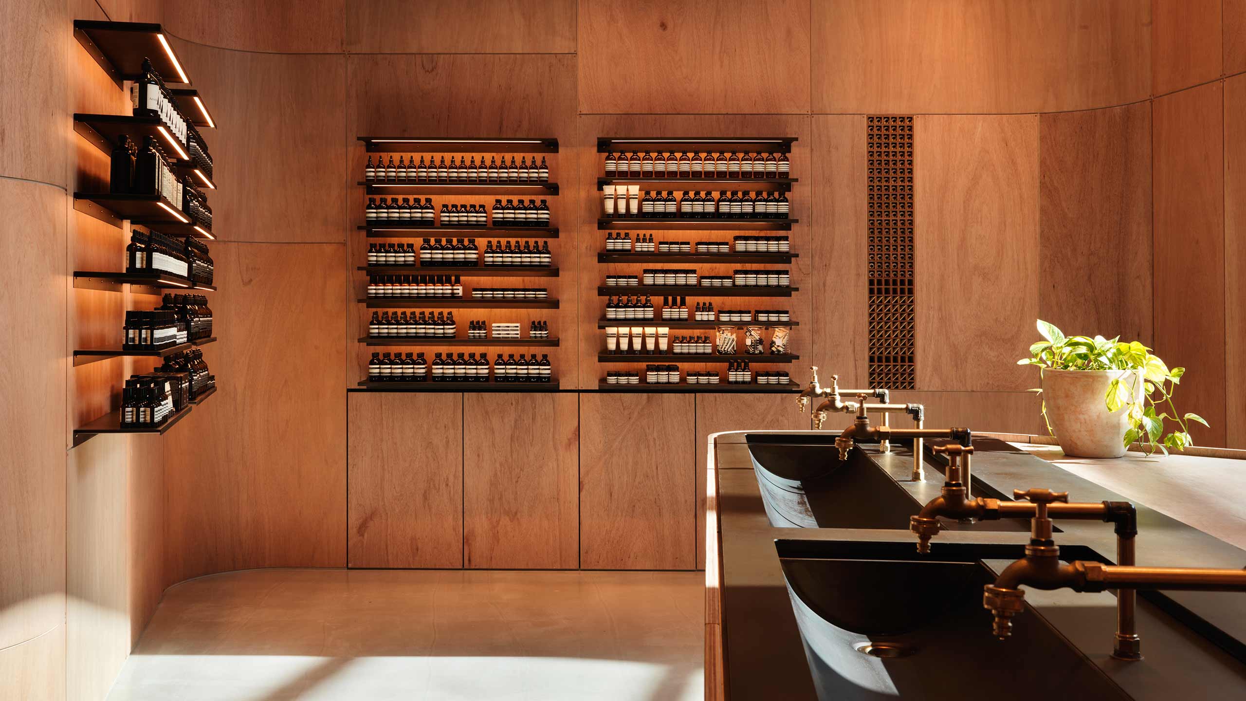 Copper fixtures and a black basin in front of a large natural timber wall that displays a number of shelves.