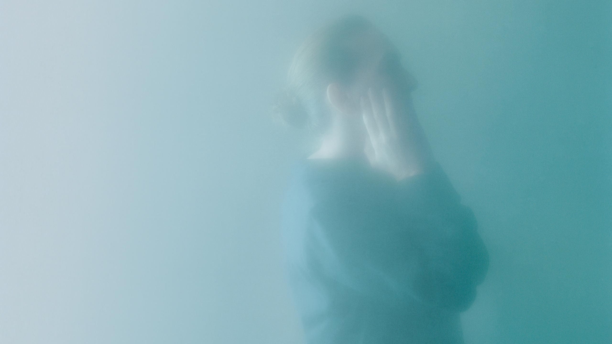 The profile of a figure applying serum to their face, obscured in a cyan haze.