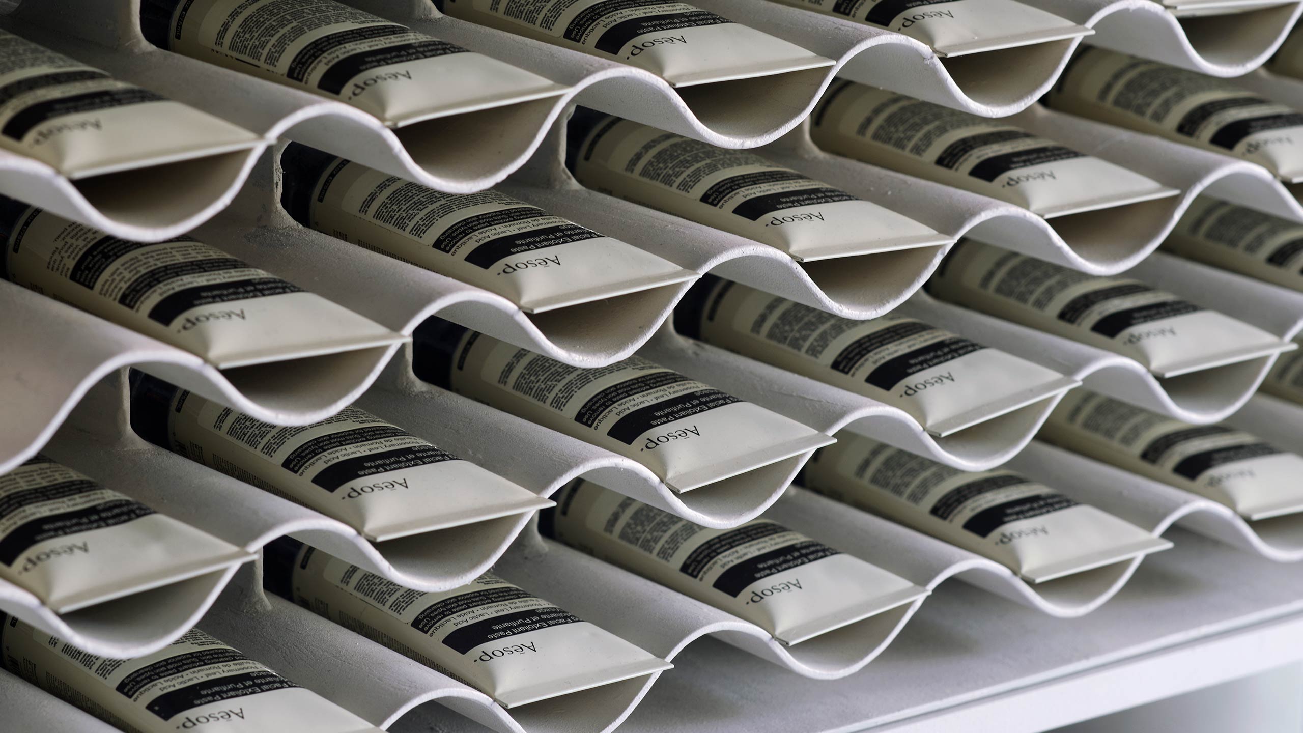 Undulating shelves containing dozens of tubes of Aesop Purifying Facial Exfoliant.