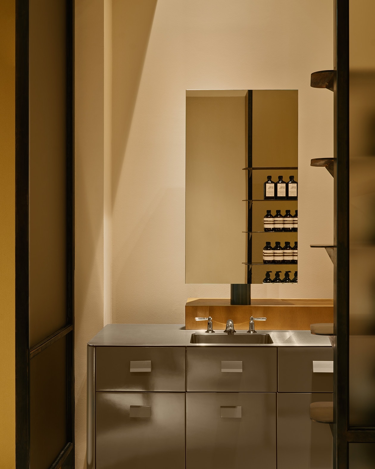 Aesop Sendlinger Strasse store interior metal basin, mirror and bathroom products display in the reflection.