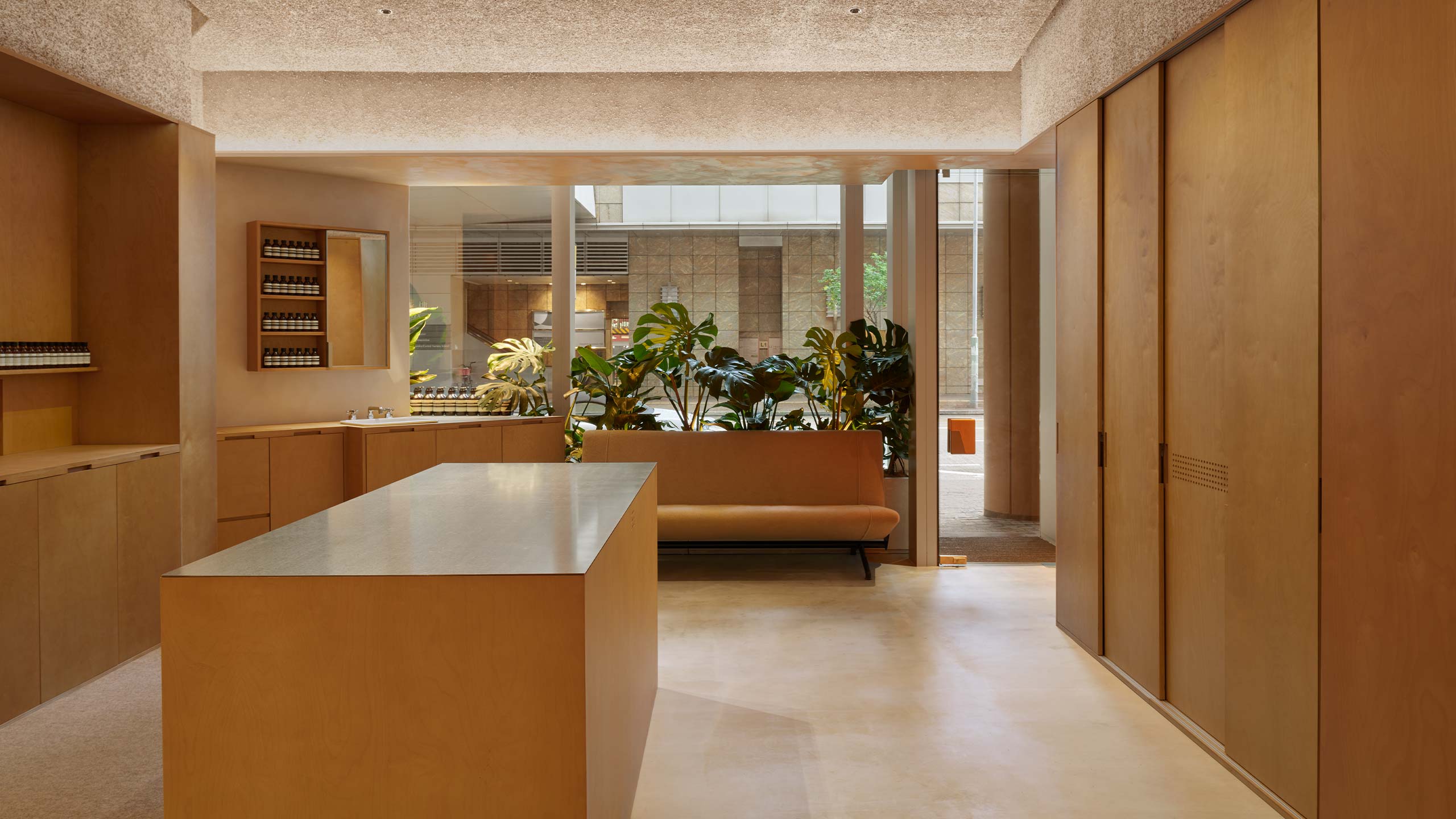 Store interior with a solitary basin, a sofa and verdant plants, next to a fragrance area.