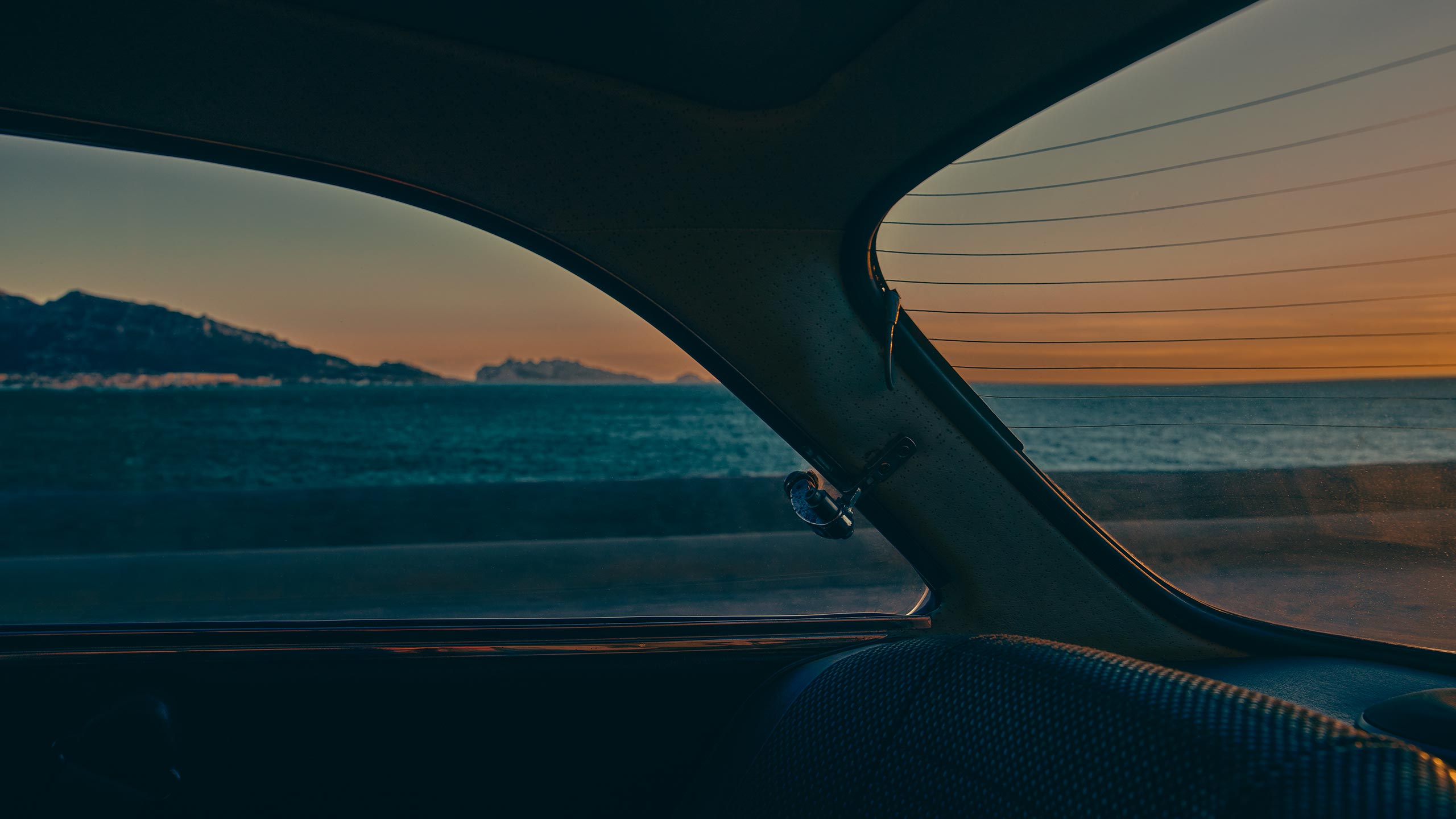 A car interior with a view of the ocean at sunset. 