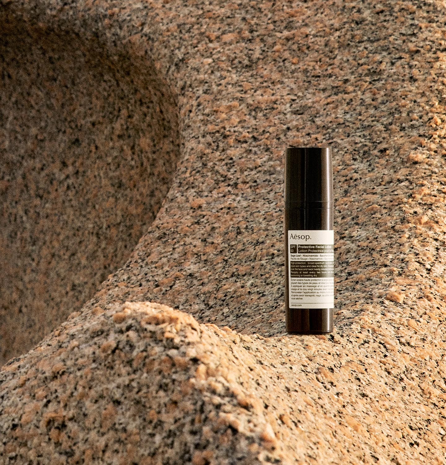 A bottle of Protective Facial Lotion SPF50 resting on a rocky shoreline.