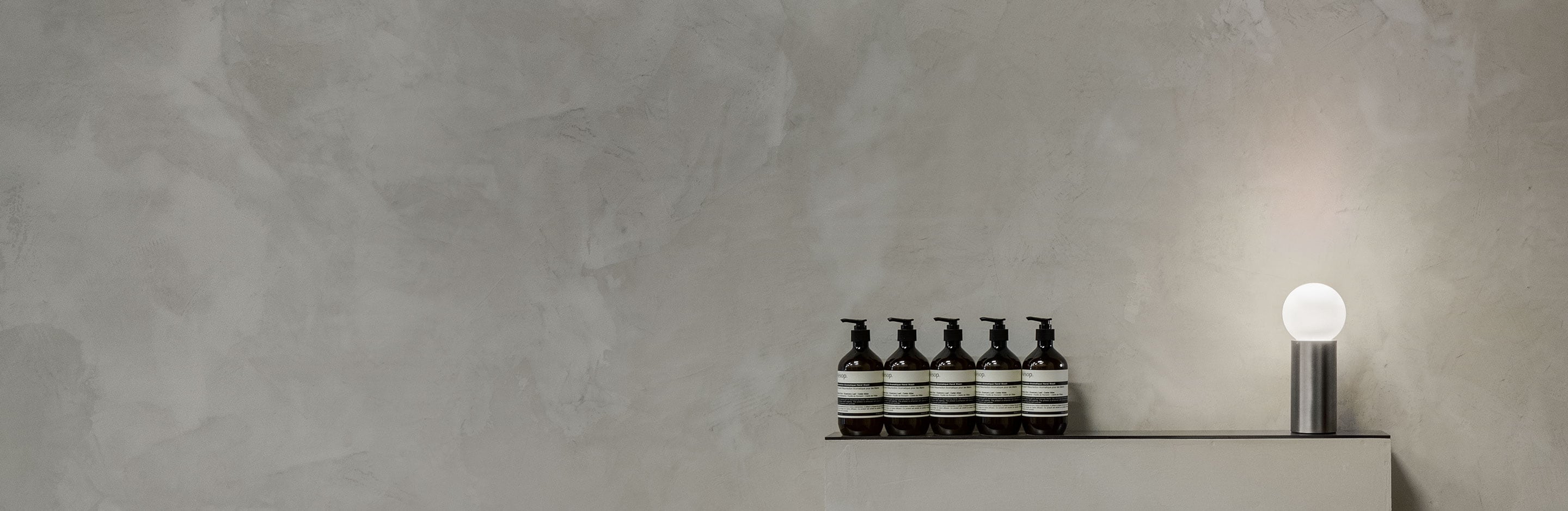 Image of Aesop products displayed along a grey wall