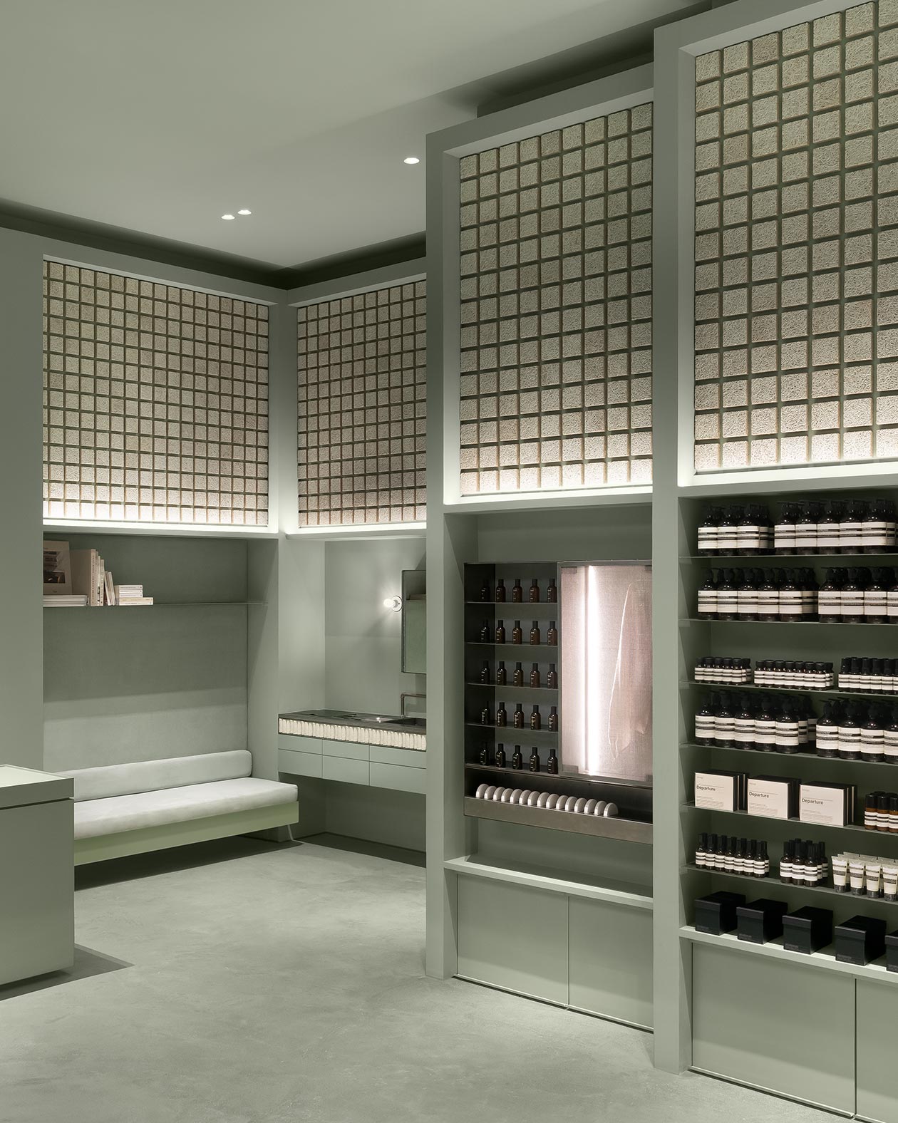 Aesop products line up on shelves in a store with tile wall