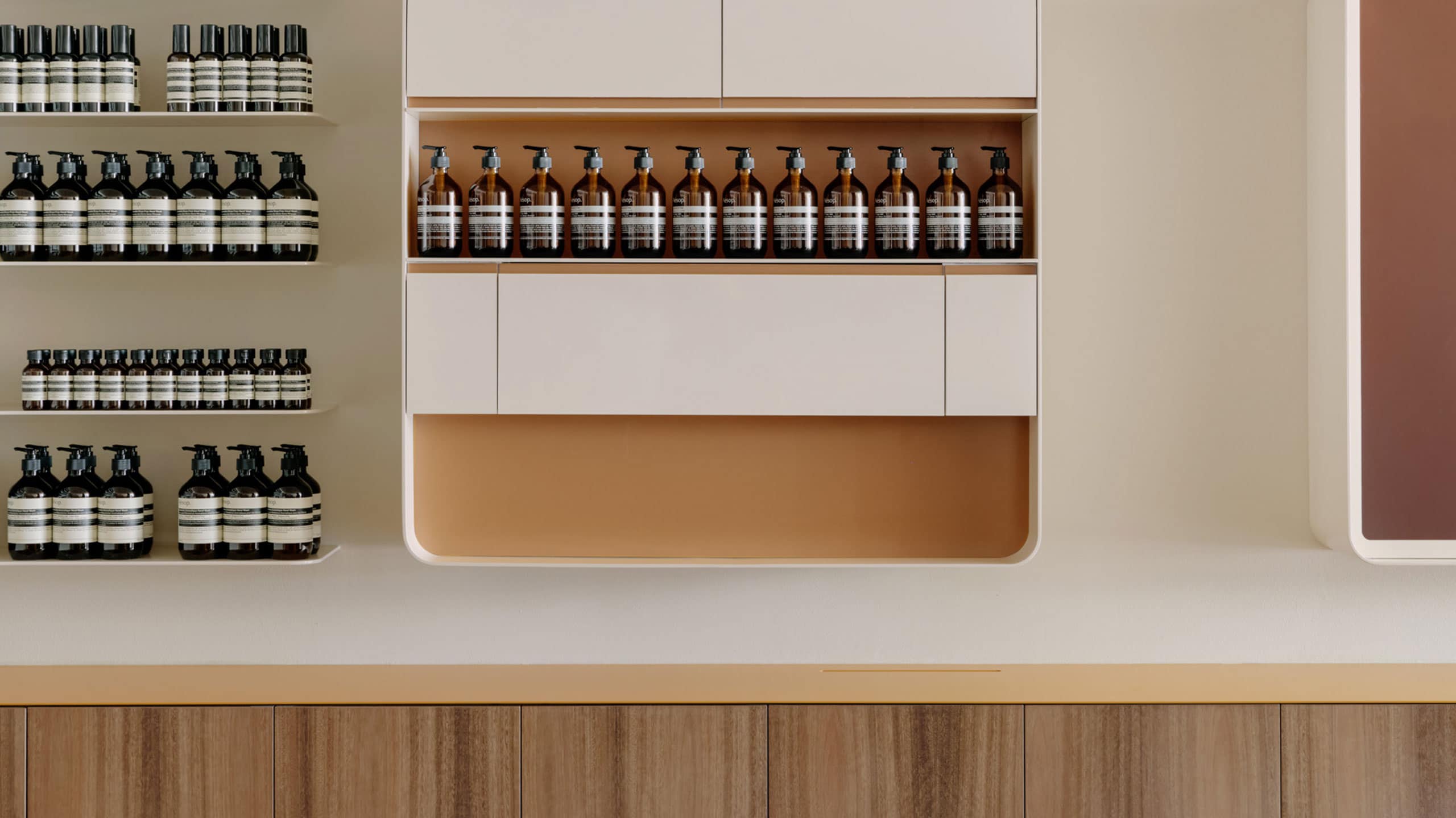 Wooden service desk in front of display featuring reusable glass Aesop bottles.