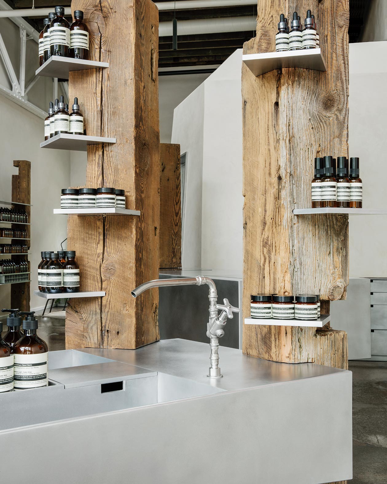 Isolated raw wooden poles hold Aesop product around a sink