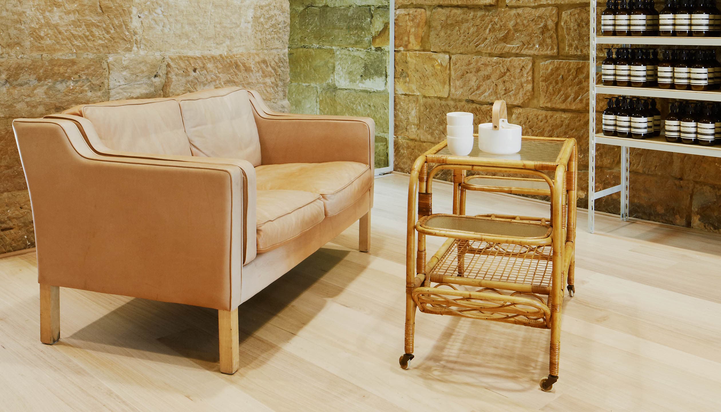 A customer space that features a tan leather sofa positioned alongside a wicker coffee table.