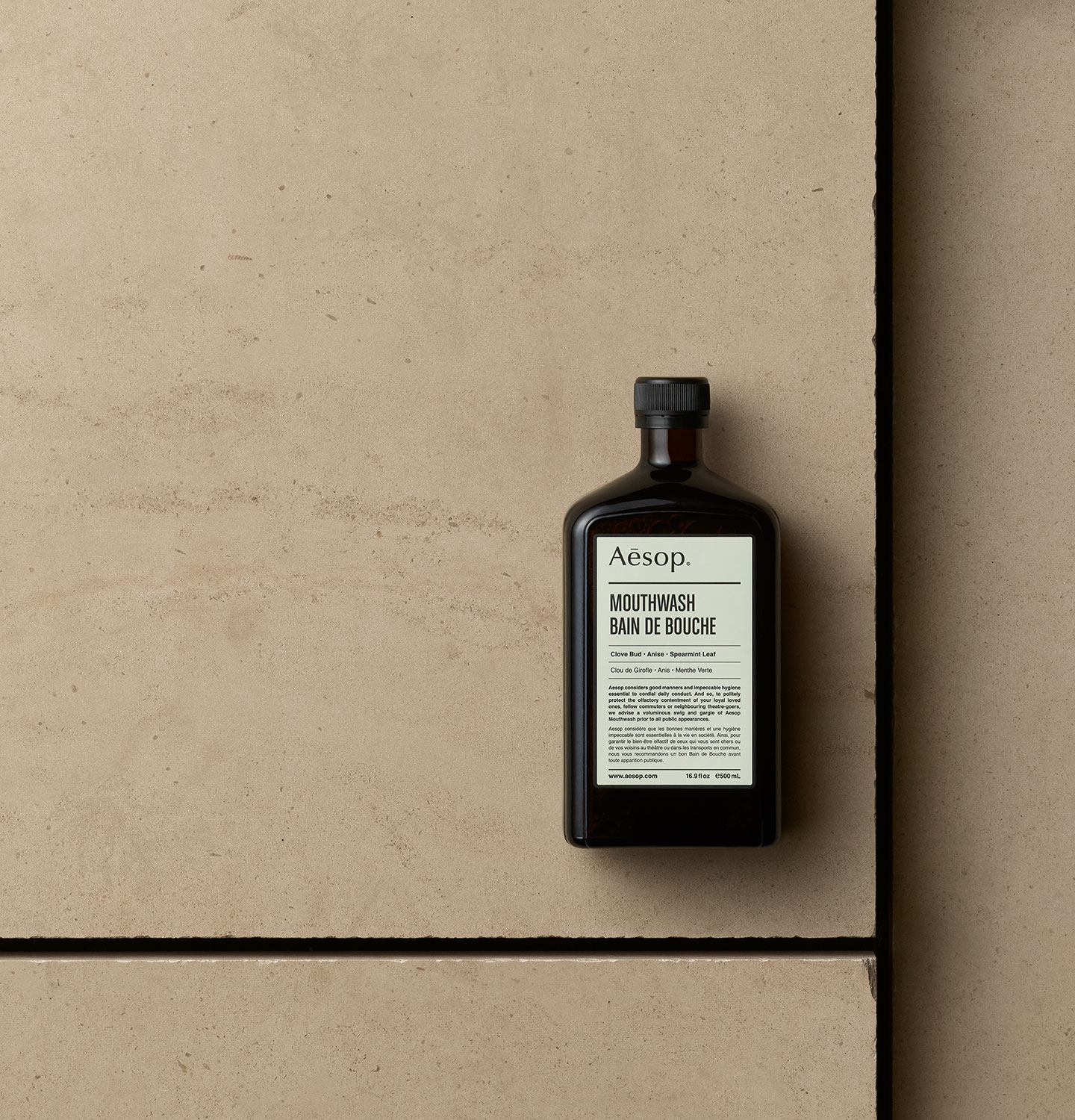 Aesop Mouthwash in amber bottle arranged on a beige textured surface.