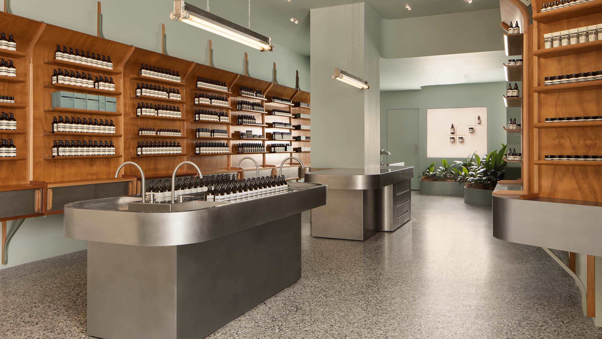 Stainless steel sink and and Aesop products placed on lacquered wood shelves
