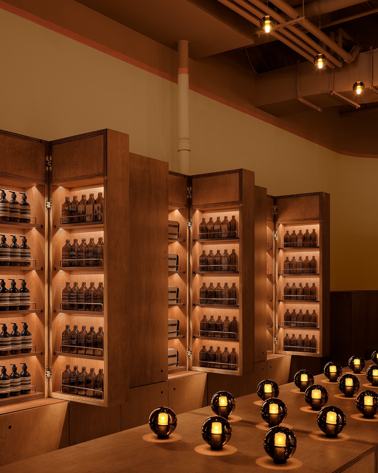 warmly lit wooden product shelves lined with products in amber glass, and a wooden center table with amber glass orb lamps arranged in a grid