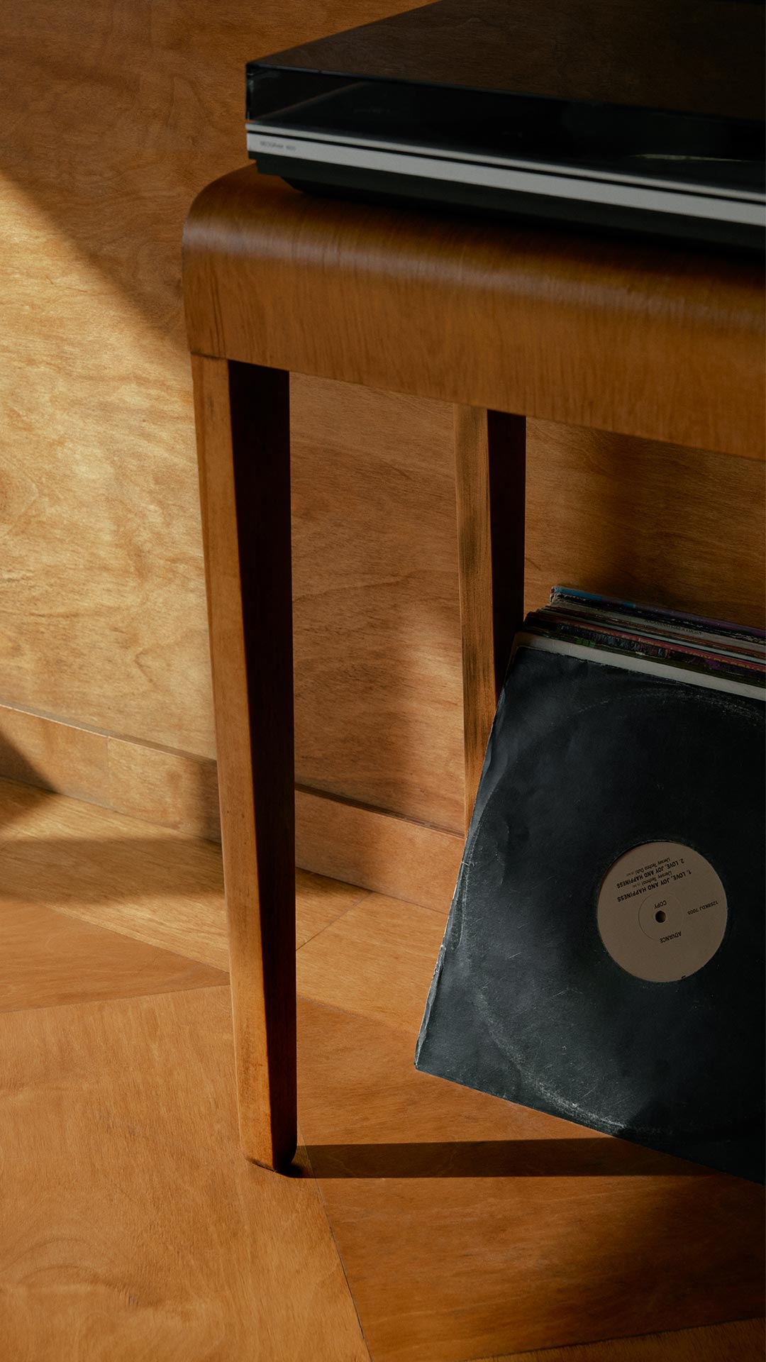 A turntable on a mid-century wooden table with a vinyl record resting beneath it.