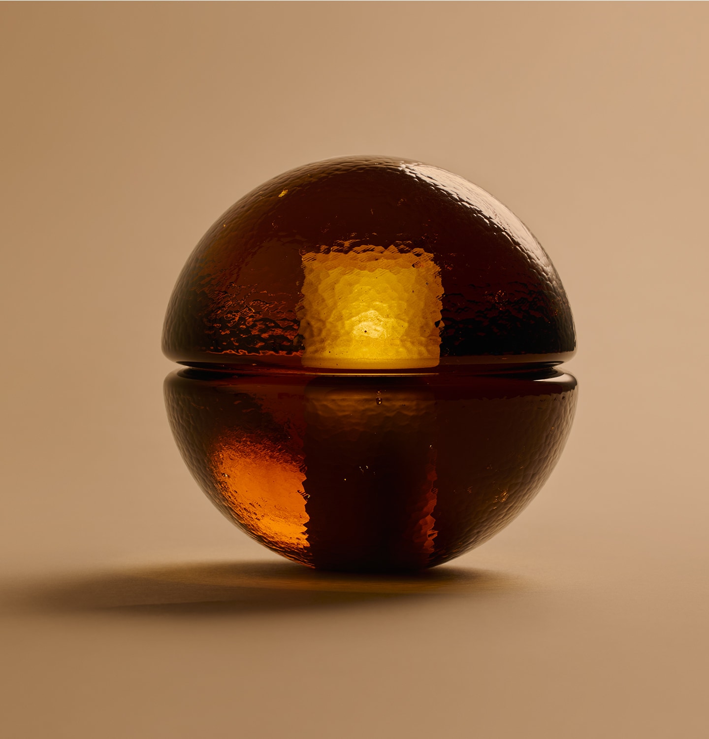 illuminated amber glass lamp in the shape of an orb, casting a shadow on a tan background