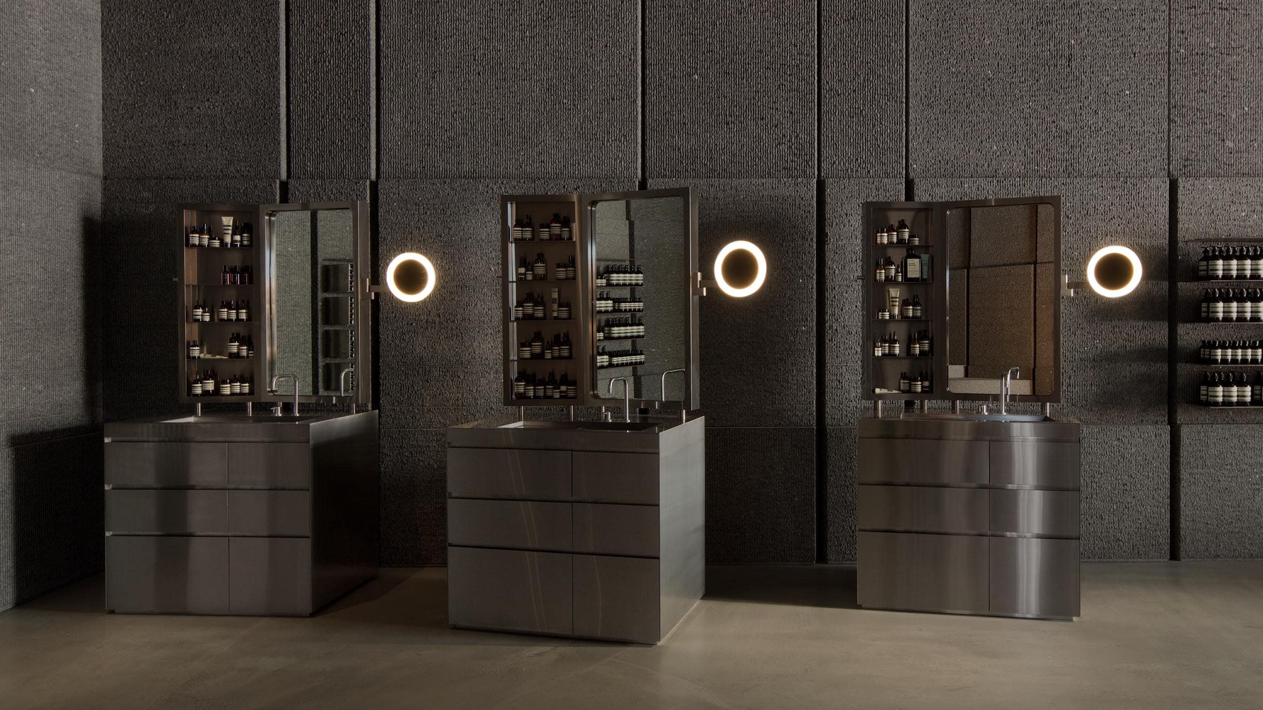 Small mirrors with ringed LED lights sit beside steel basins