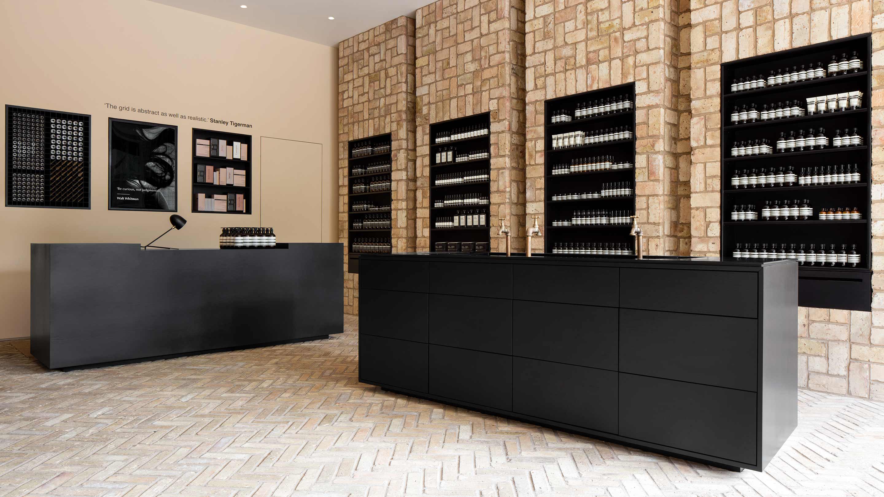 Black steel cabinets sitting on brick floor; brick walls fitted with steel shelves holding Aesop product.