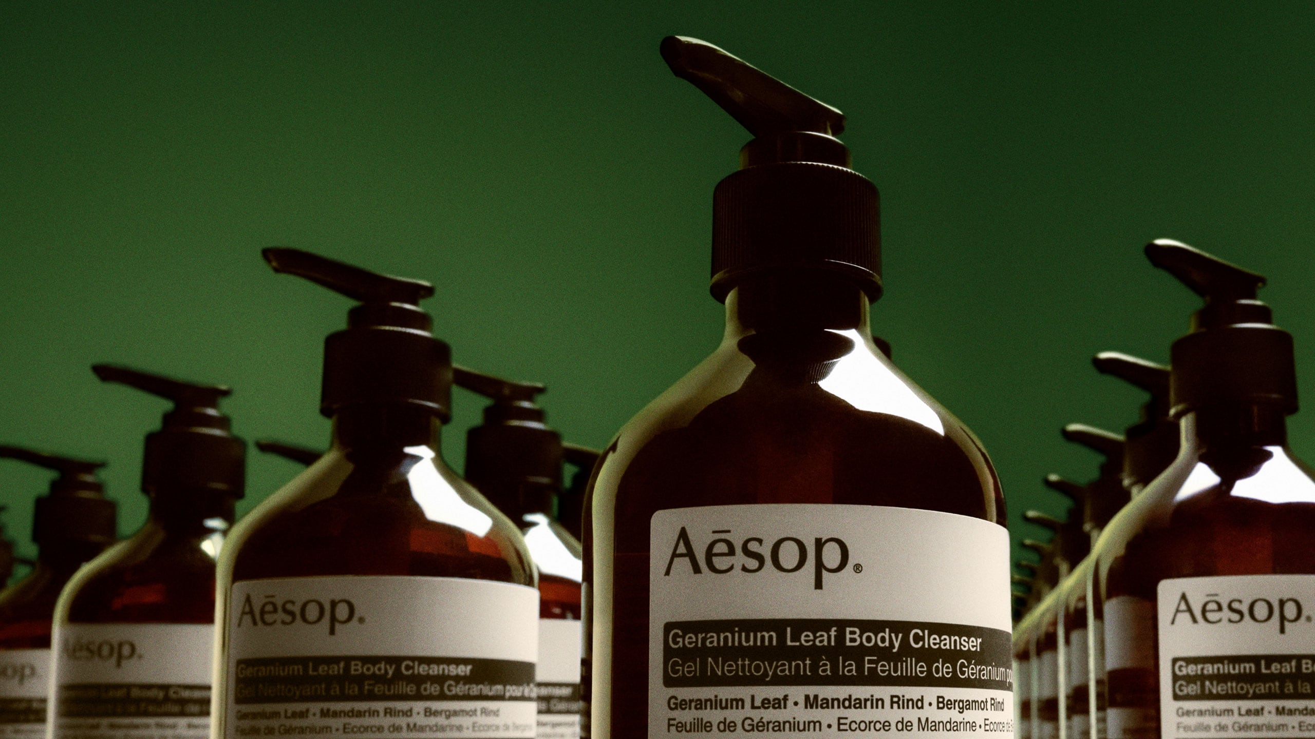 A close-up view of multiple Geranium Leaf Body Cleanser, arranged in a line against a green background.