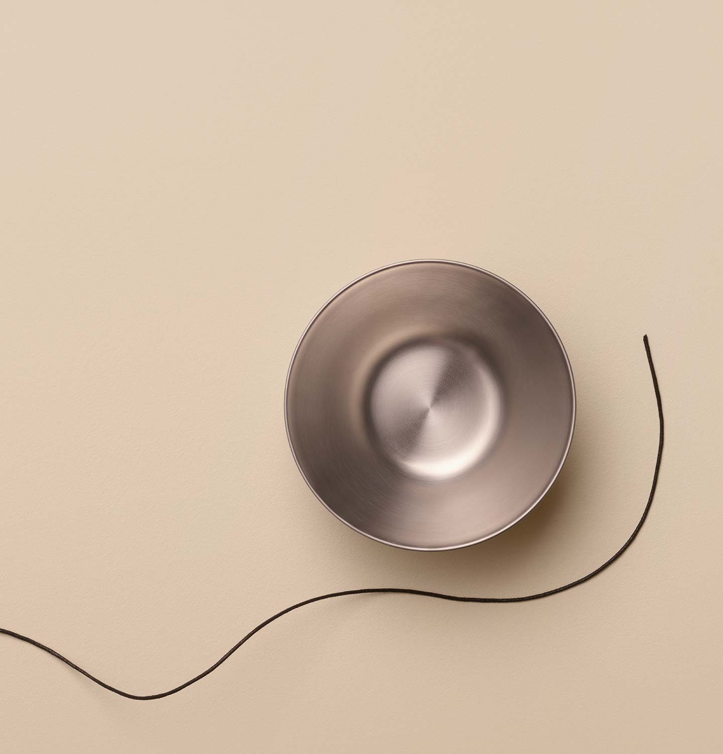 Aesop Stainless Steel Bowl arranged alongside a dark string on a beige textured surface.