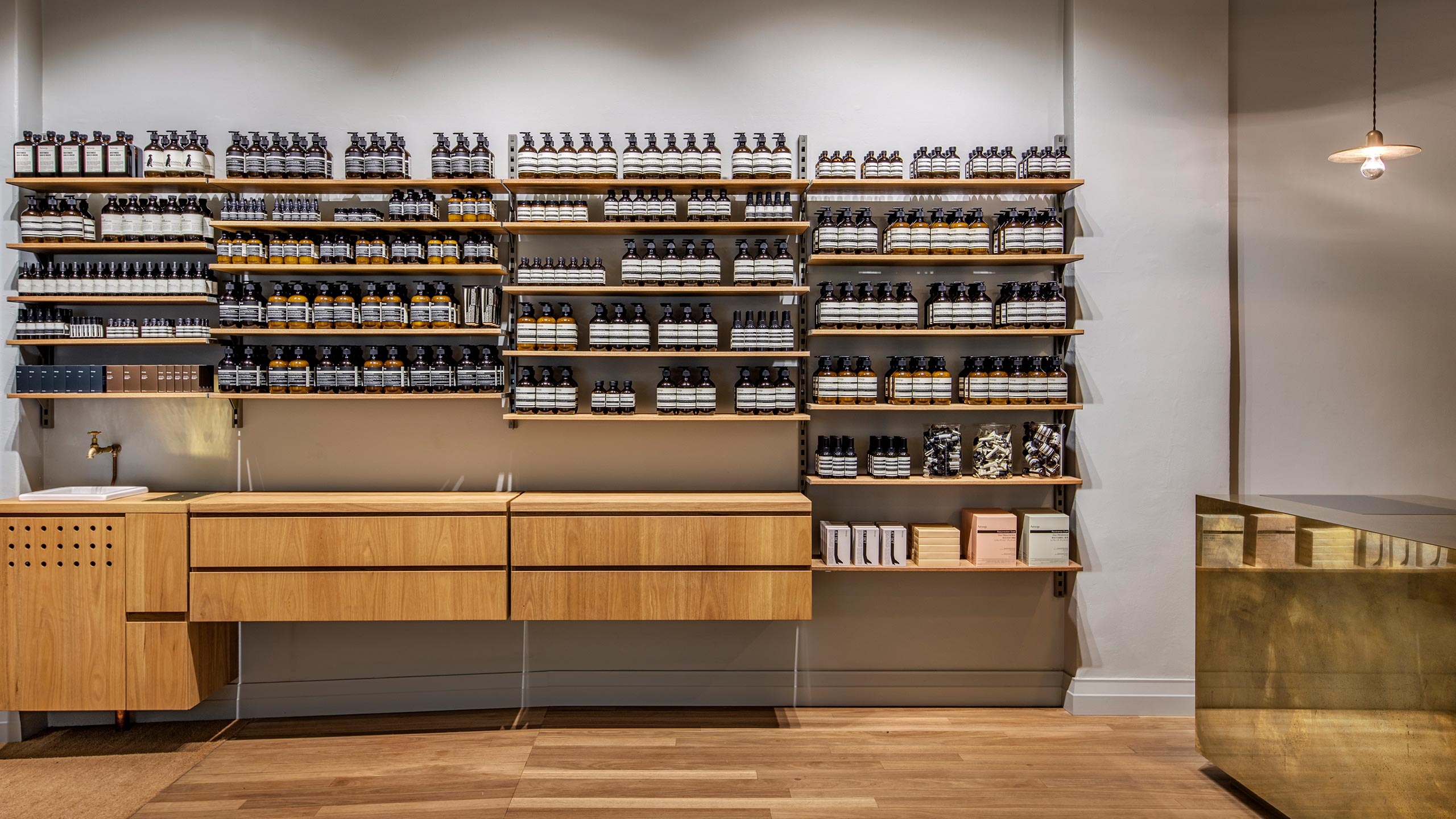 Wooden shelves that display Aesop products, above a customer service basin and wooden drawers.